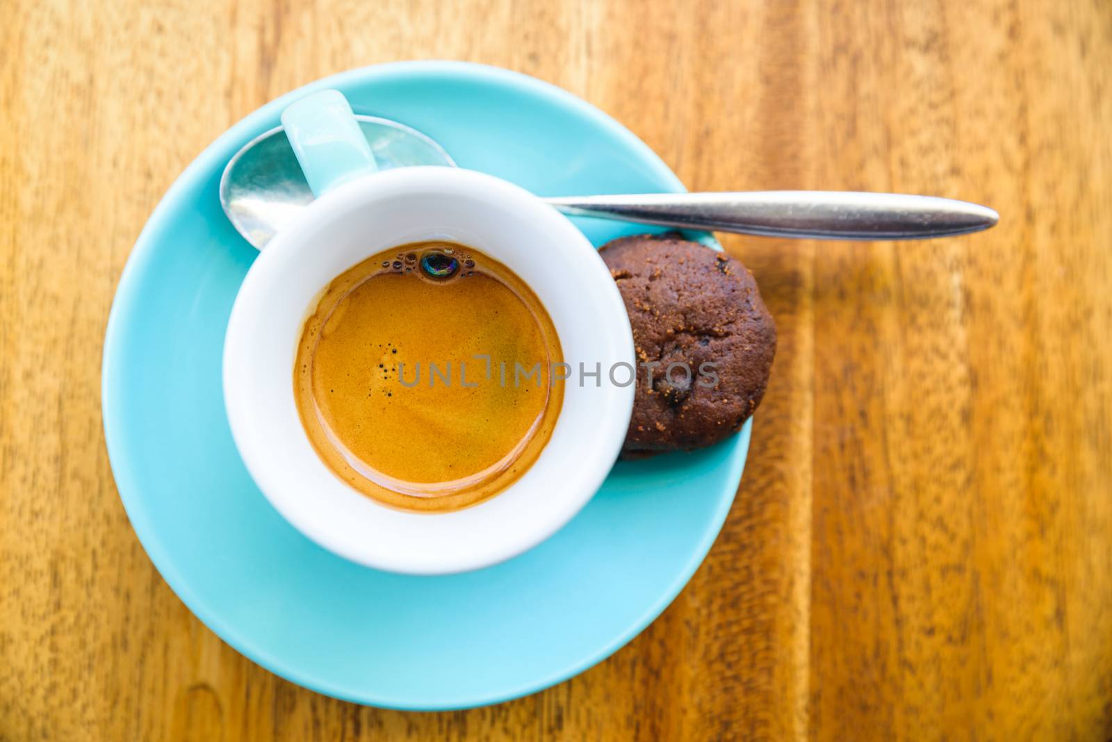 An espresso served with a chocolate cookie in a turquoise cup on a wood table