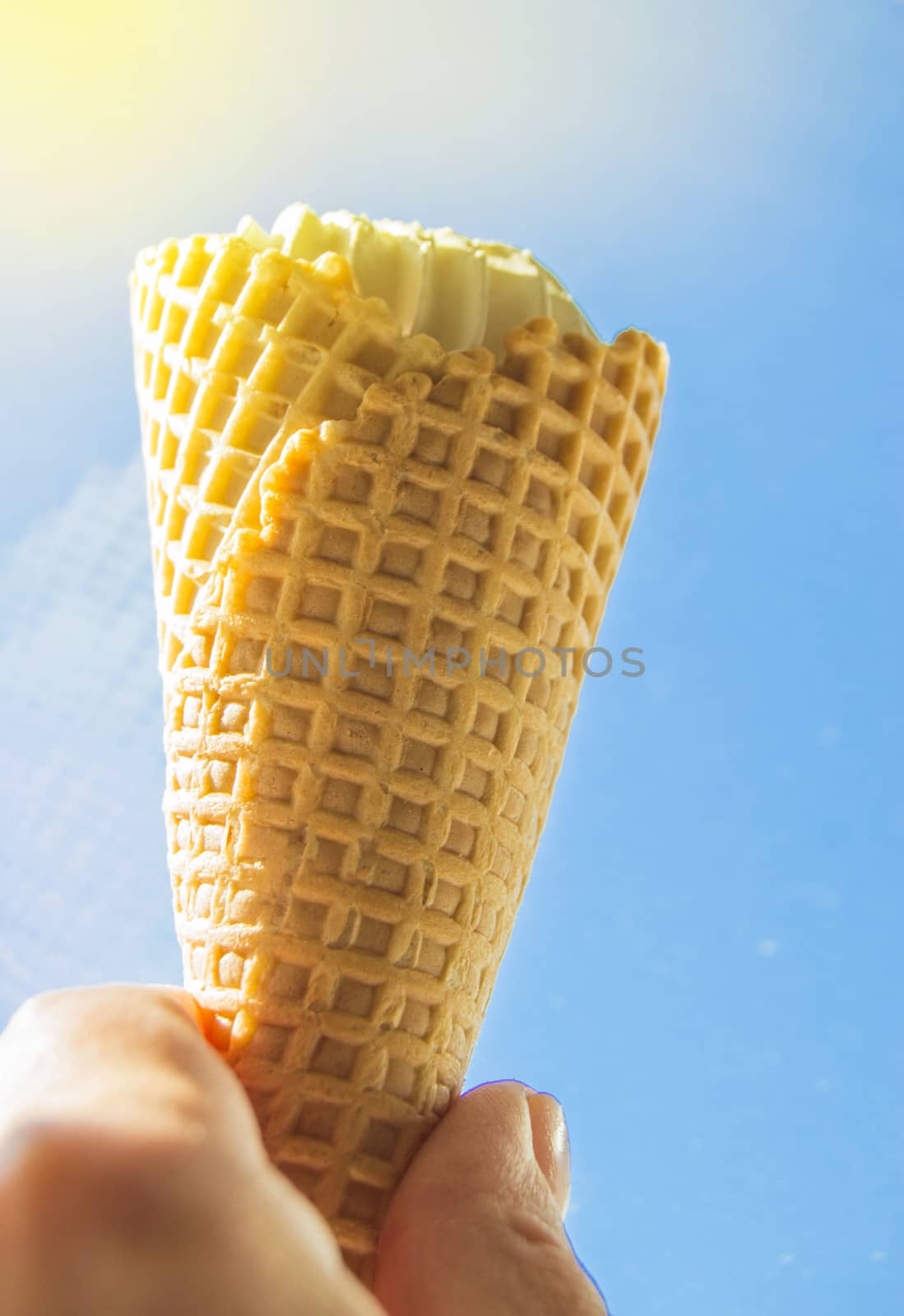 Summer, party, hand holding a vanilla ice cream cone against the blue sky and sunlight.