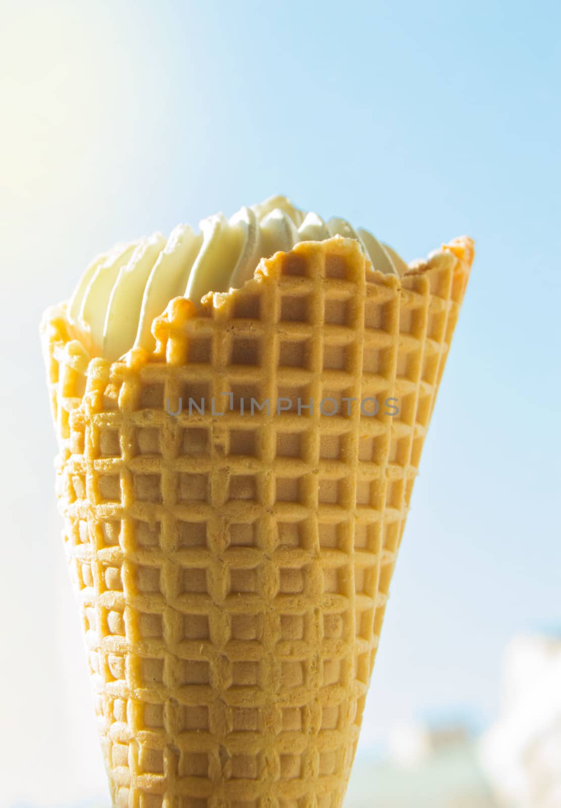 Vanilla ice cream cone against blue sky and sunlight.