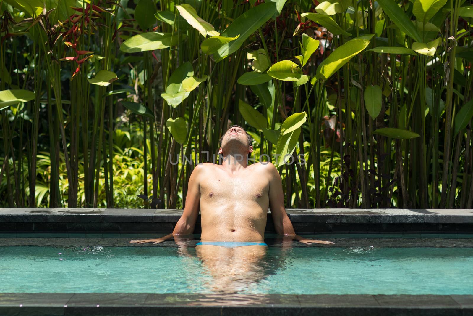 Man relaxing in outdoor spa infinity swimming pool surrounded with lush tropical greenery of Ubud, Bali. Male wellness, natural beauty and body care concept.