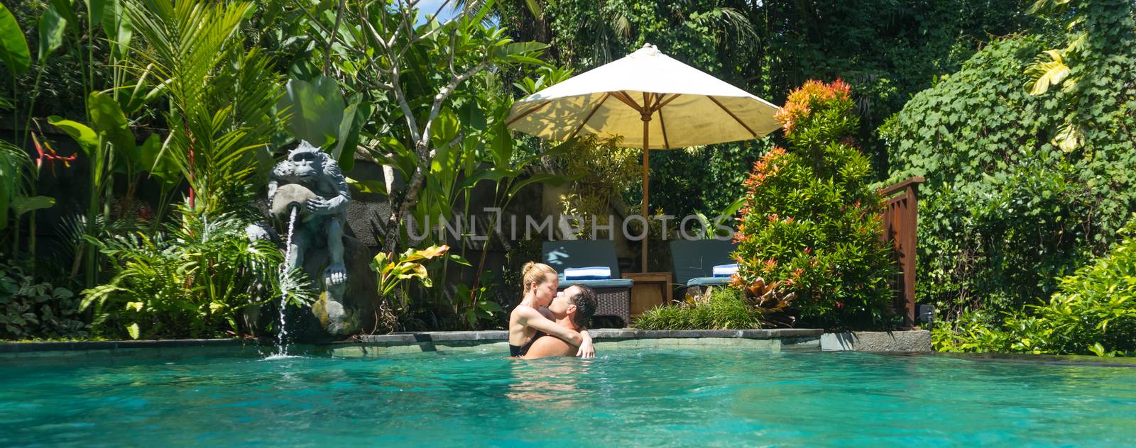 Happy couple kissing while relaxing in outdoor spa infinity swimming pool surrounded with lush tropical greenery of Ubud, Bali. Luxury spa and wellness vacation retreat concept by kasto