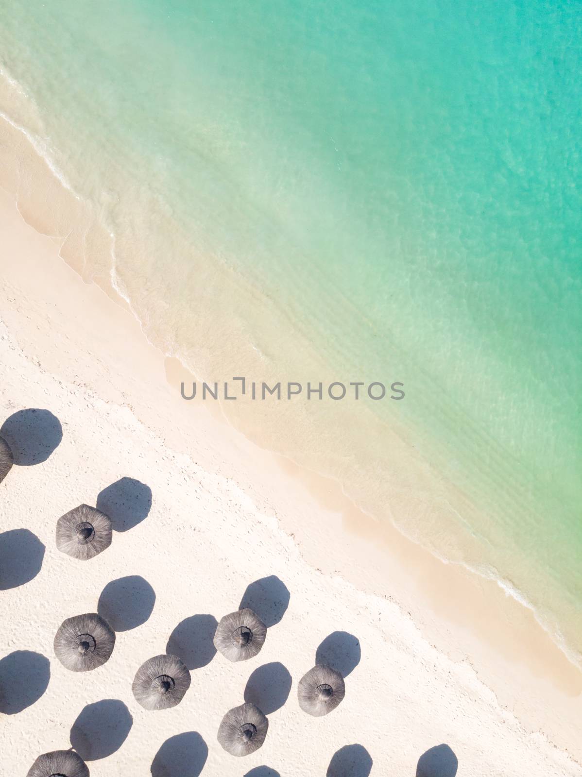 Aerial view of amazing tropical white sandy beach with palm leaves umbrellas and turquoise sea, Mauritius.