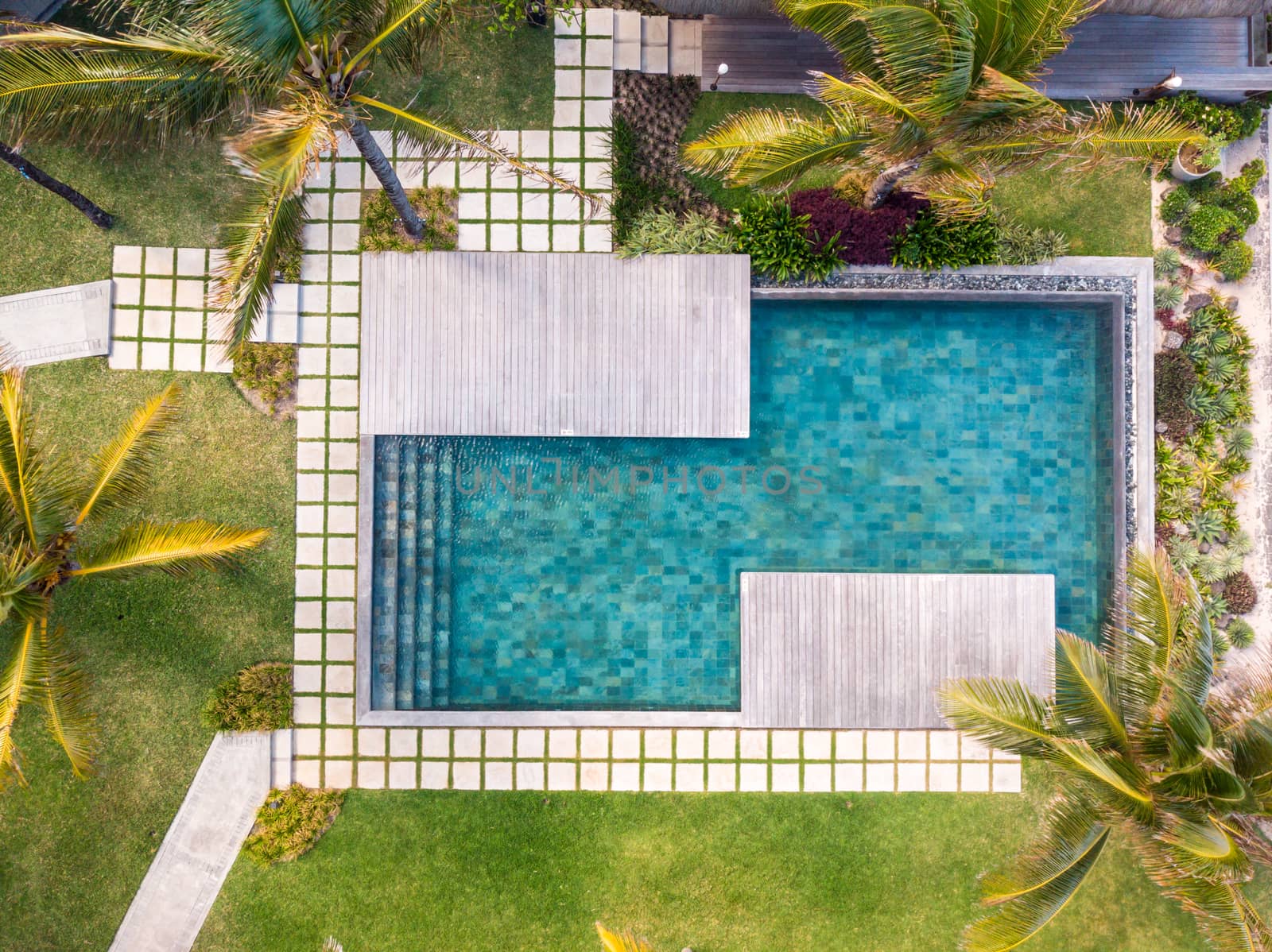 Aerial view of luxury hotel resort with swimming pool with stair and wooden deck surrounded by palm trees. Paradise destination for vacations.