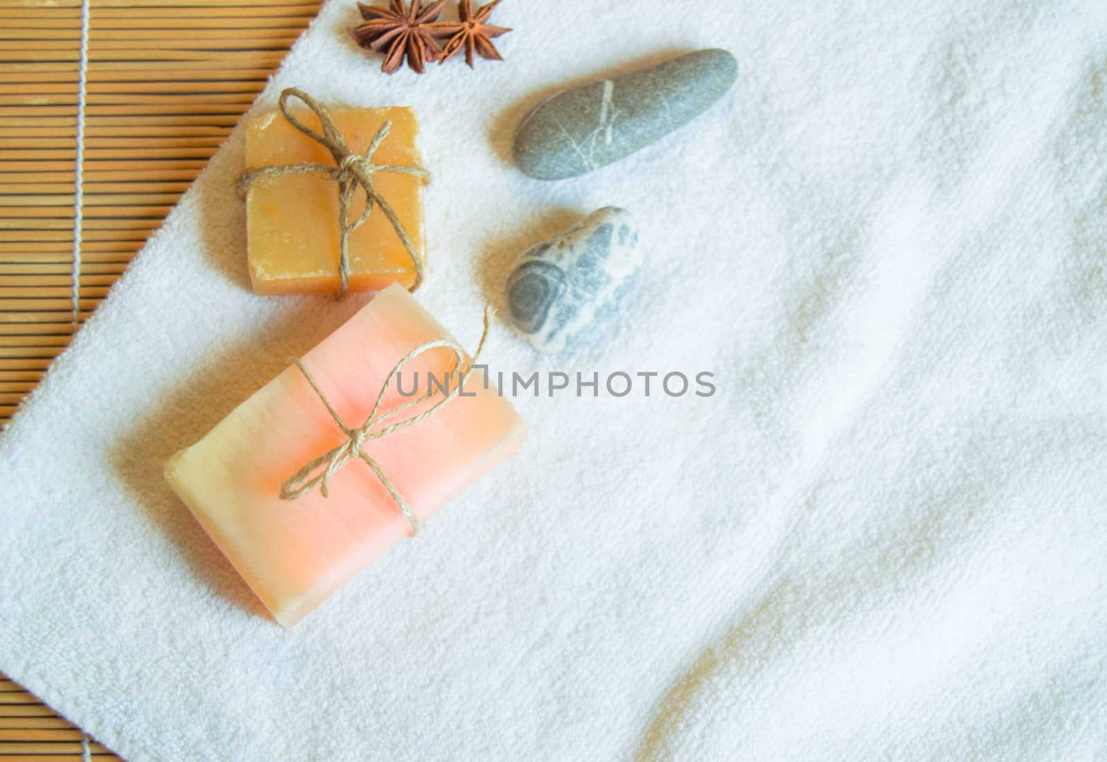 Spa setting with white towel, handmade soap, stones, on natural bamboo background, flat lay copy space.