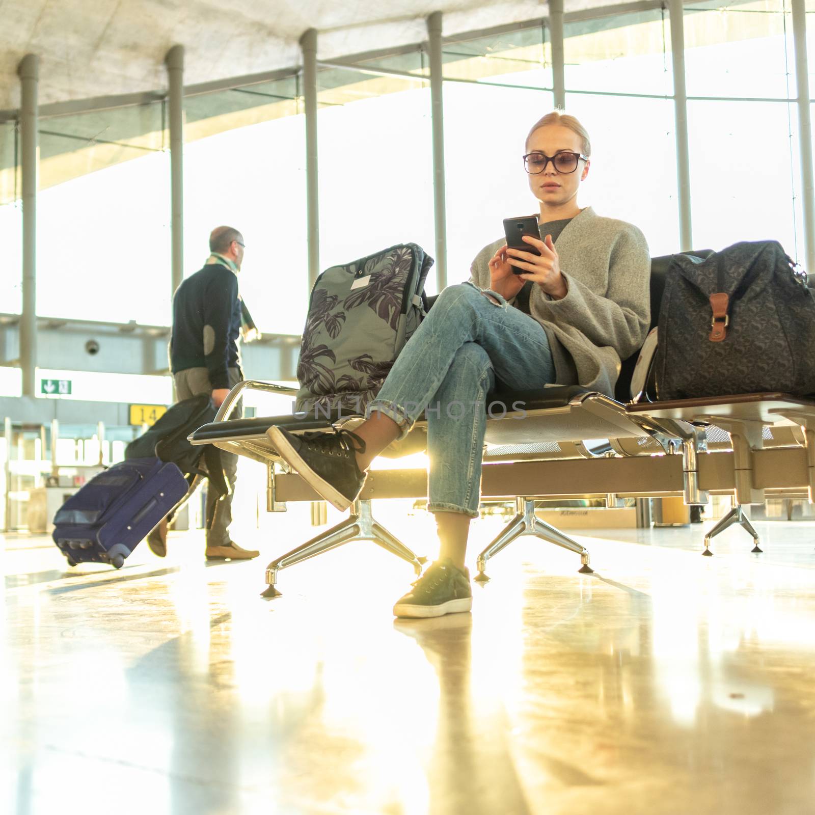 Female traveler using her cell phone while waiting to board a plane at departure gates at airport terminal. by kasto