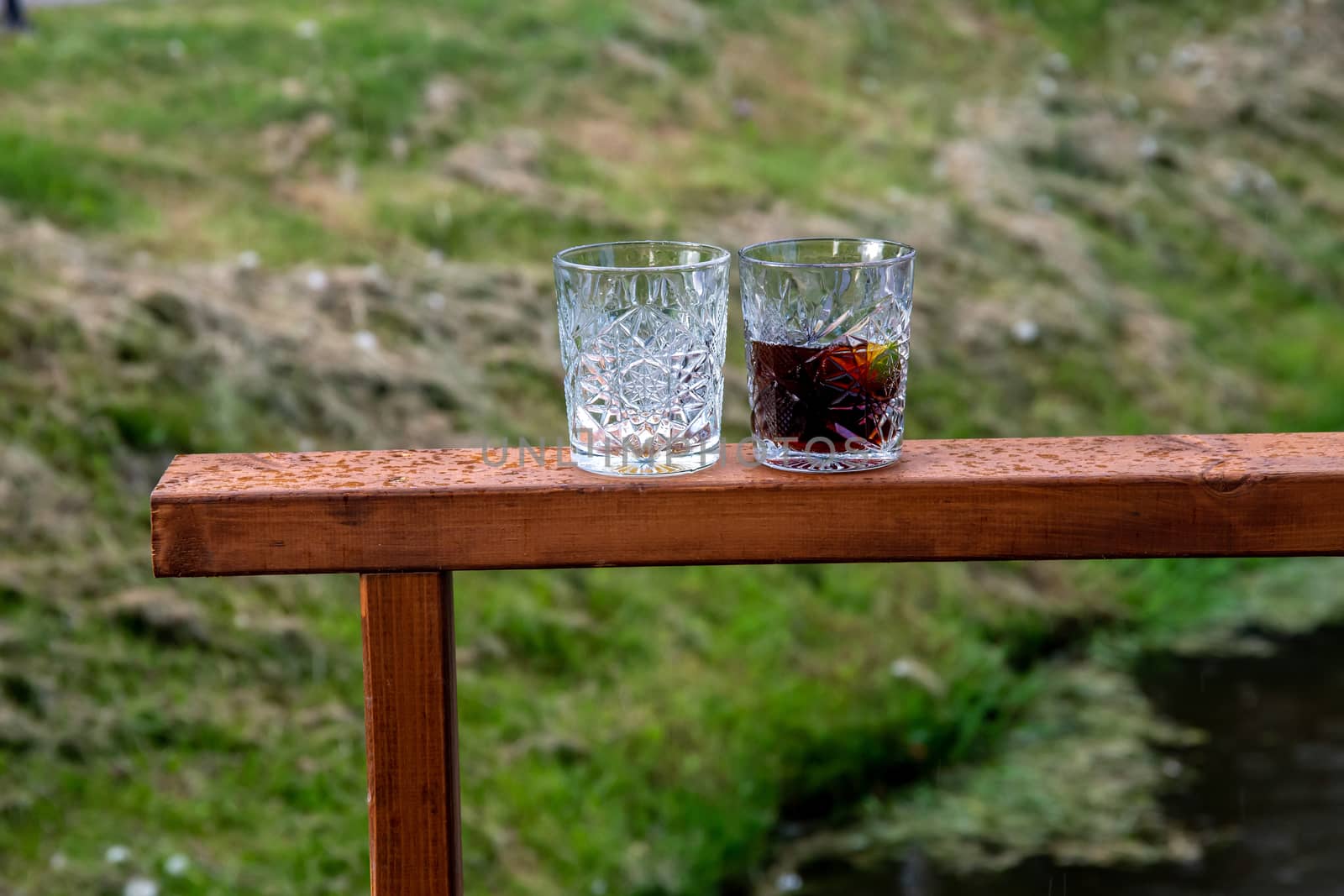 Two whiskey glasses on a wooden frame outdoors. Two glasses of  whiskey on green grass background.