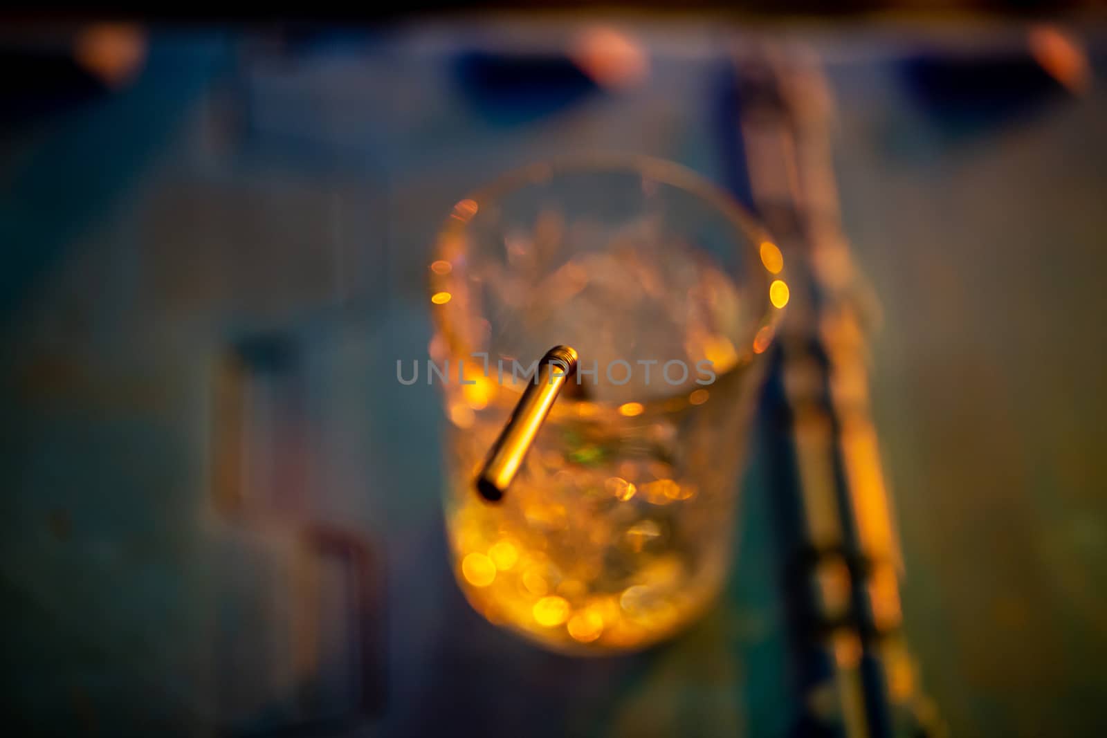 Closeup of abstract cocktail glass with straw on multicolor background. Glass of drink in multicolored light.