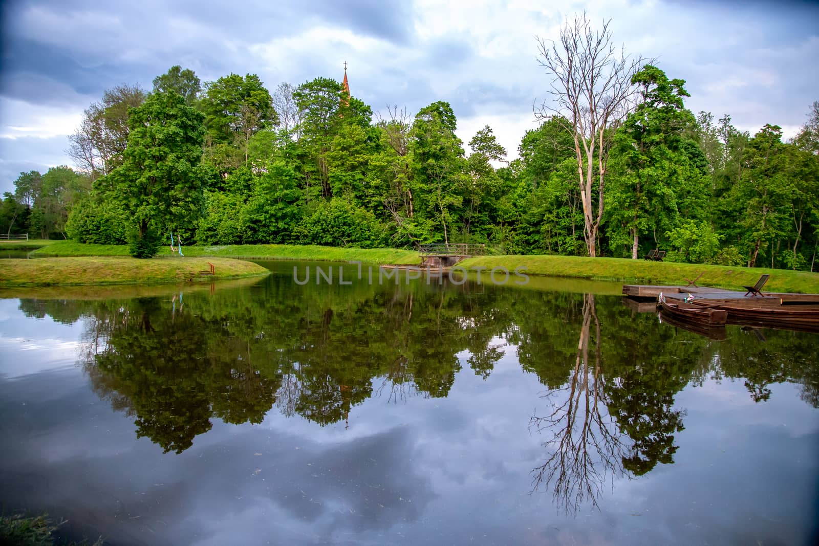 View on summer landscape of pond and trees in sunny day. Reflection of summer trees and clouds in water. Landscape with trees, boat pier and river. 