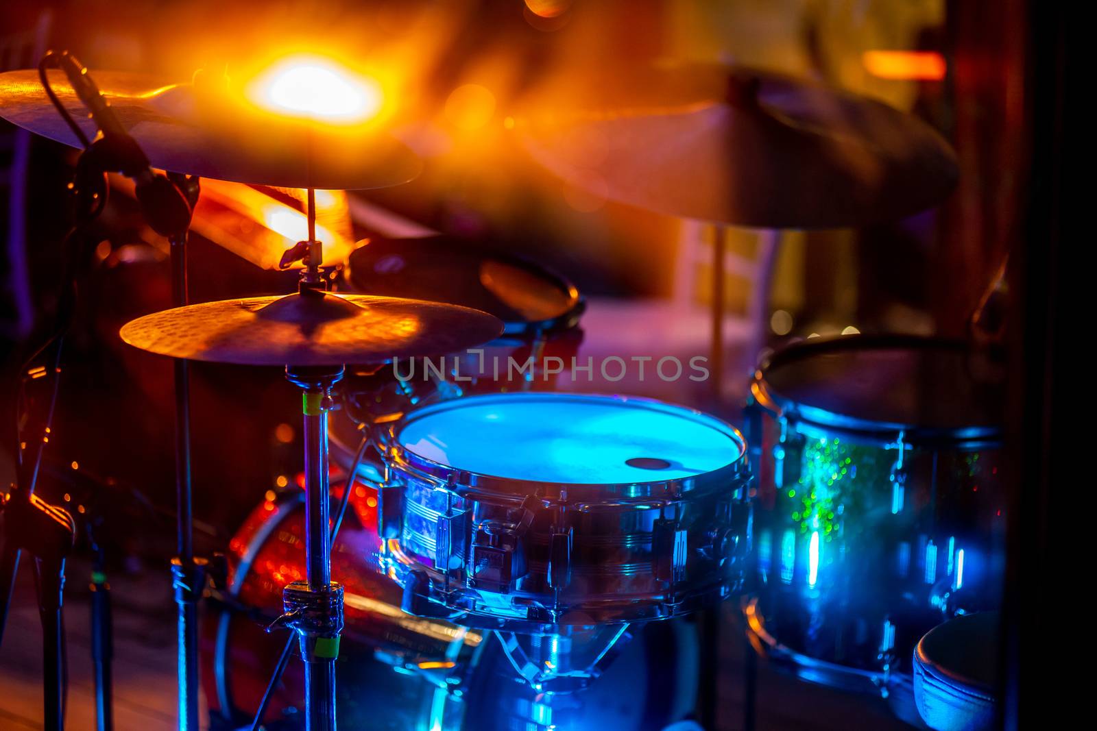 Empty abstract light illuminated stage with drumkit and microphone. Drums in multicolored light during celebrations on stage.