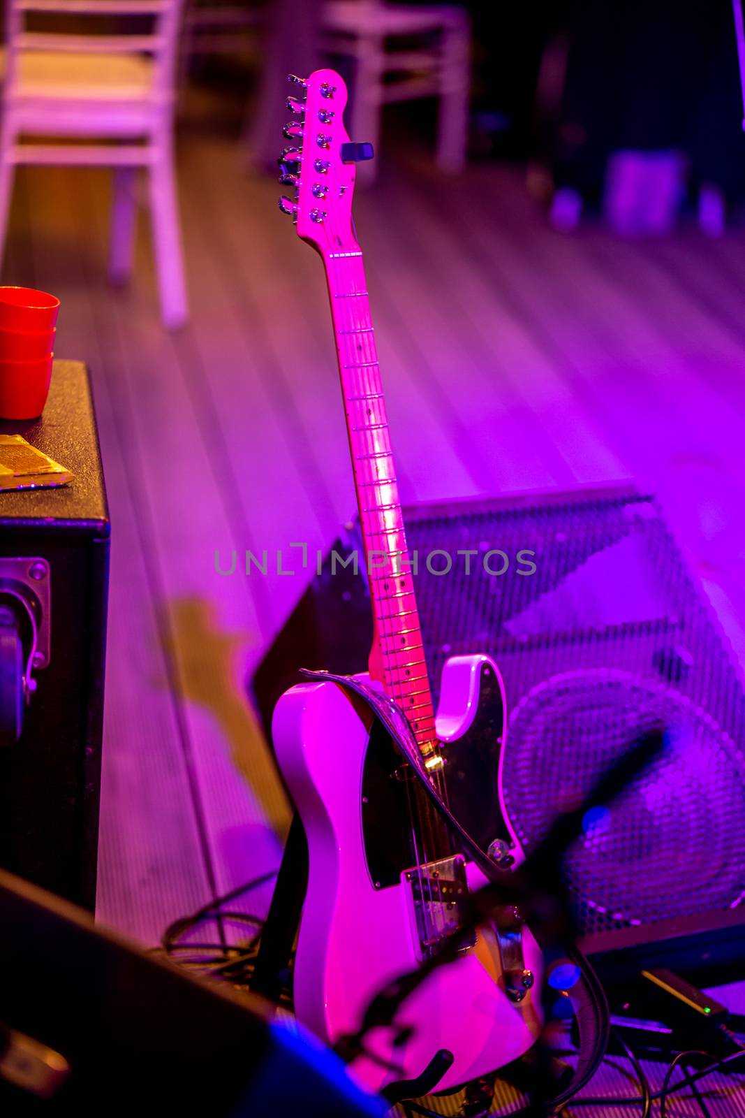 Electric guitar and sound amplifier in multicolored light during celebrations on stage. Empty abstract light illuminated stage with electric guitar and sound amplifier