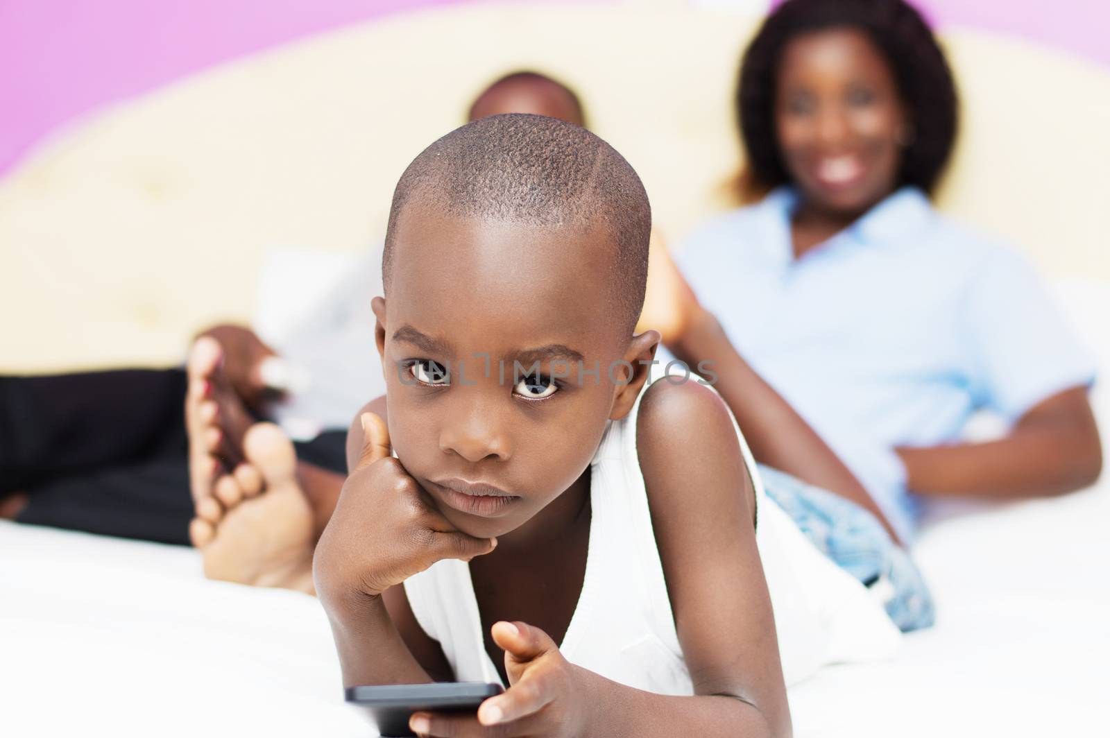 child plays with mobile phone of his parents who are watching in the background smiling .