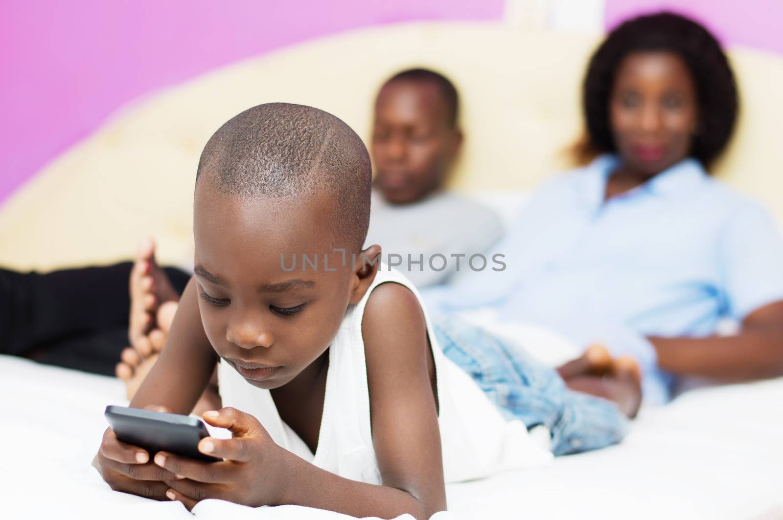child plays with mobile phone of his parents who are watching in the background smiling .