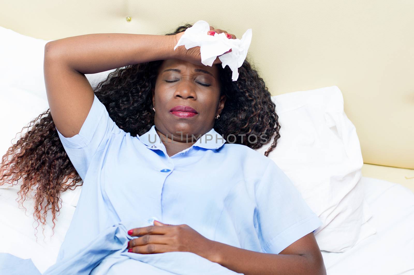 sick African woman lying in bed holding white handkerchief in hand