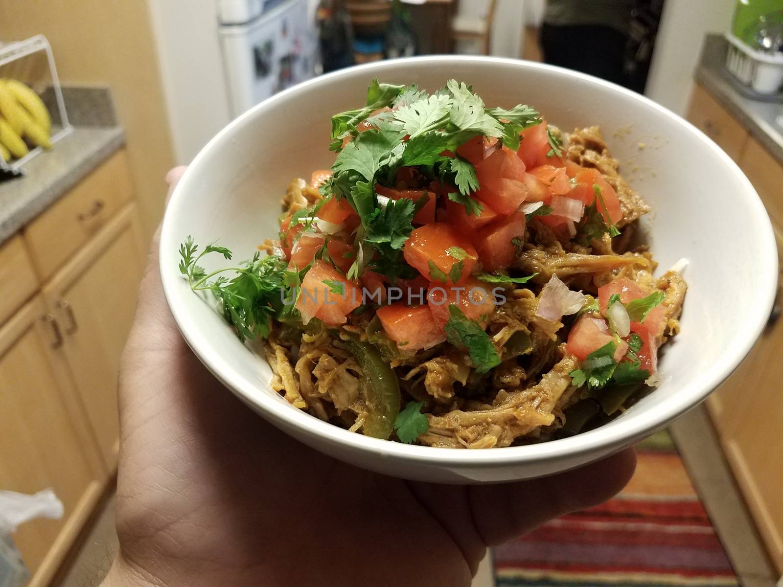 hand holding bowl of pulled pork and tomato and cilantro in kitchen