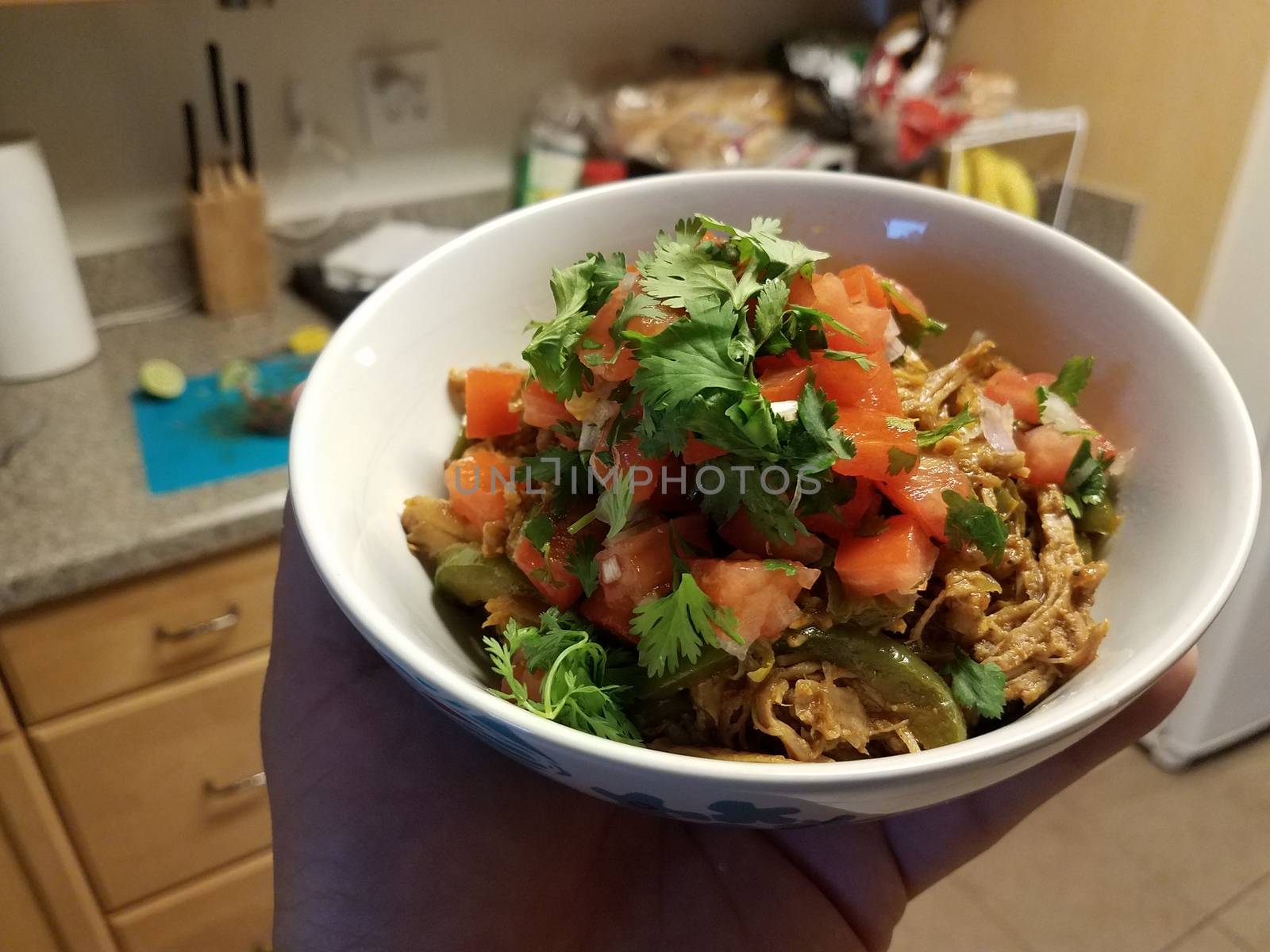 hand holding bowl of pulled pork and tomato and cilantro in kitchen