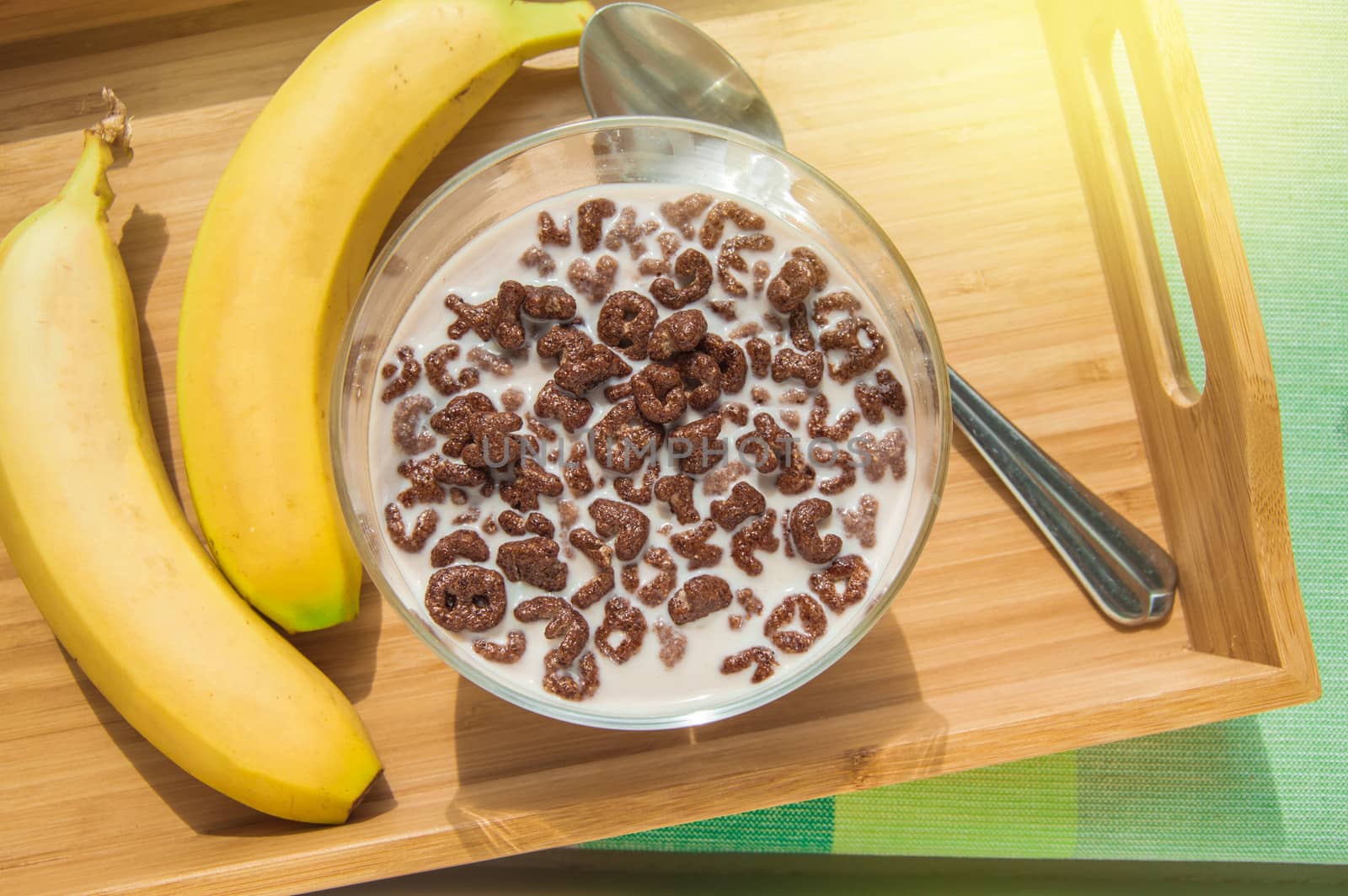 Bowl of oatmeal chocolate flakes in the shape of letters of the alphabet with milk on a wooden tray with bananas, healthy Breakfast concept for children and adults