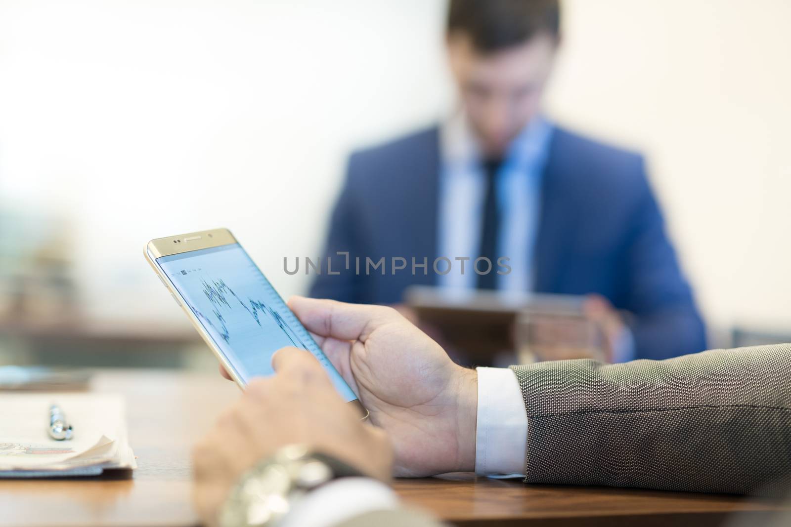 Close up of a businessman reviewing data on smart phone at working business meeting in corporative office. Focus on mobile device.
