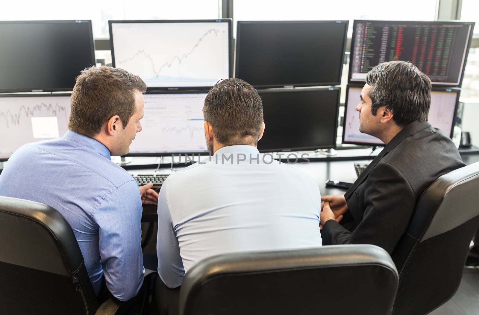 Businessmen brainstorming while looking at data on multiple computer screens in corporate office. Business people trading online. Business, entrepreneurship and team work concept.