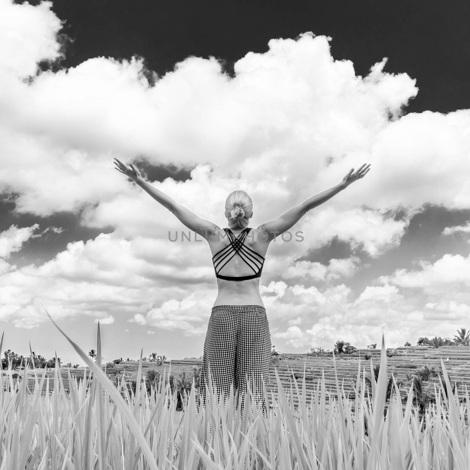 Relaxed healthy woman, arms rised, enjoying pure nature at beautiful green rice fields on Bali. Concept of healthy and clean environment, ecology, balance in life, freedom, happiness, and well being.