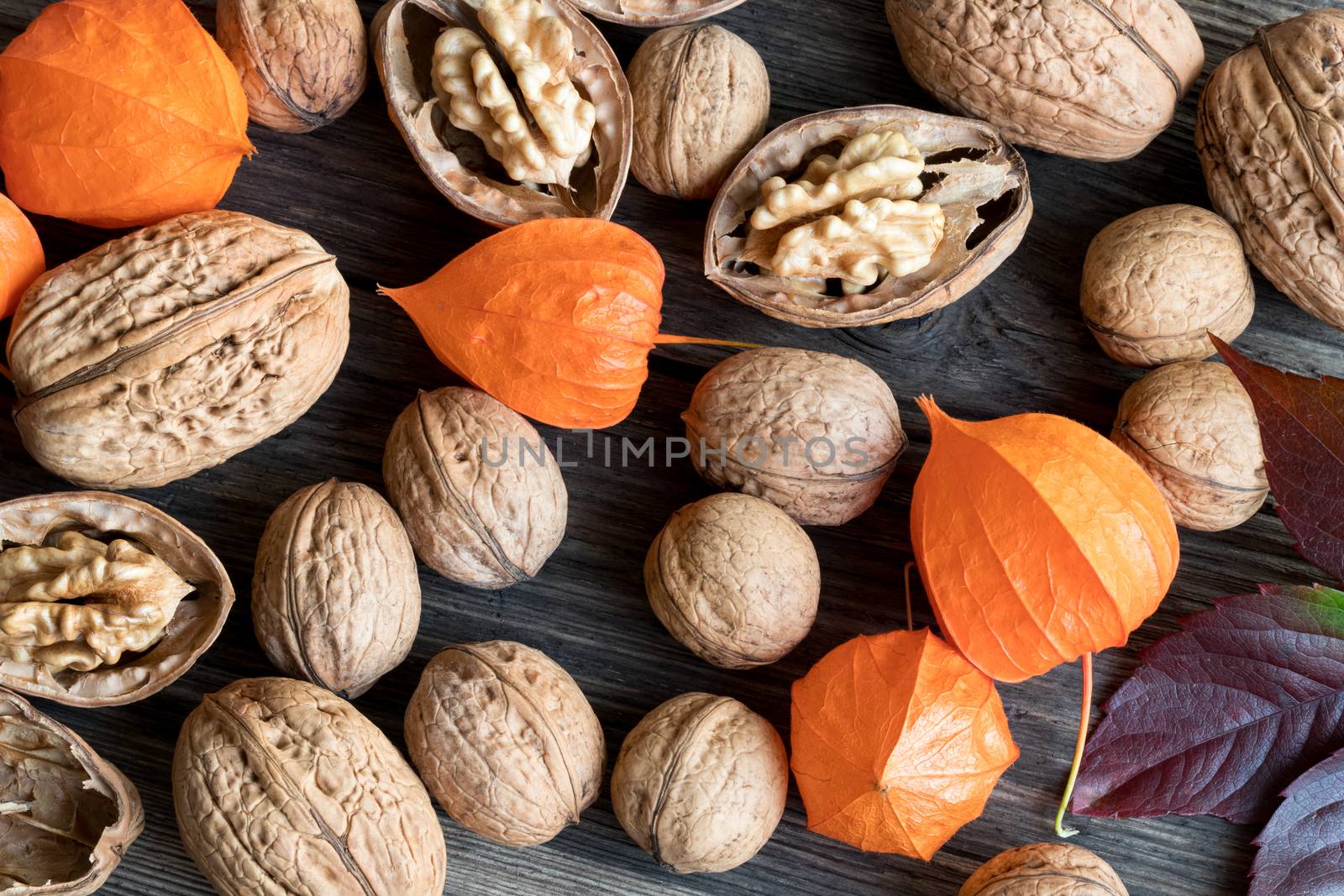 Whole and broken walnuts, Physalis alkekengi (Chinese lantern) and autumn leaves on a wooden background, top view