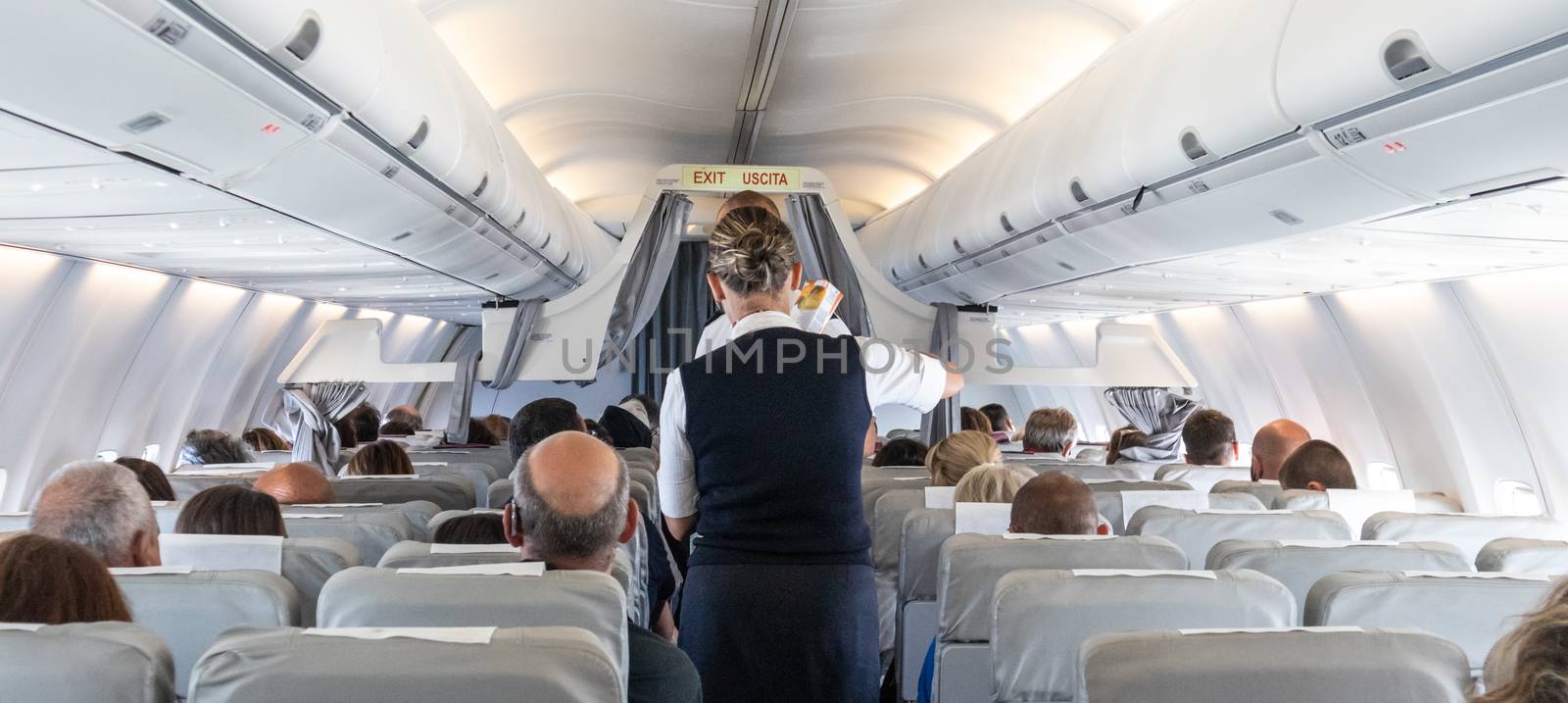 Interior of commercial airplane with stewardess serving passengers on seats during flight. by kasto