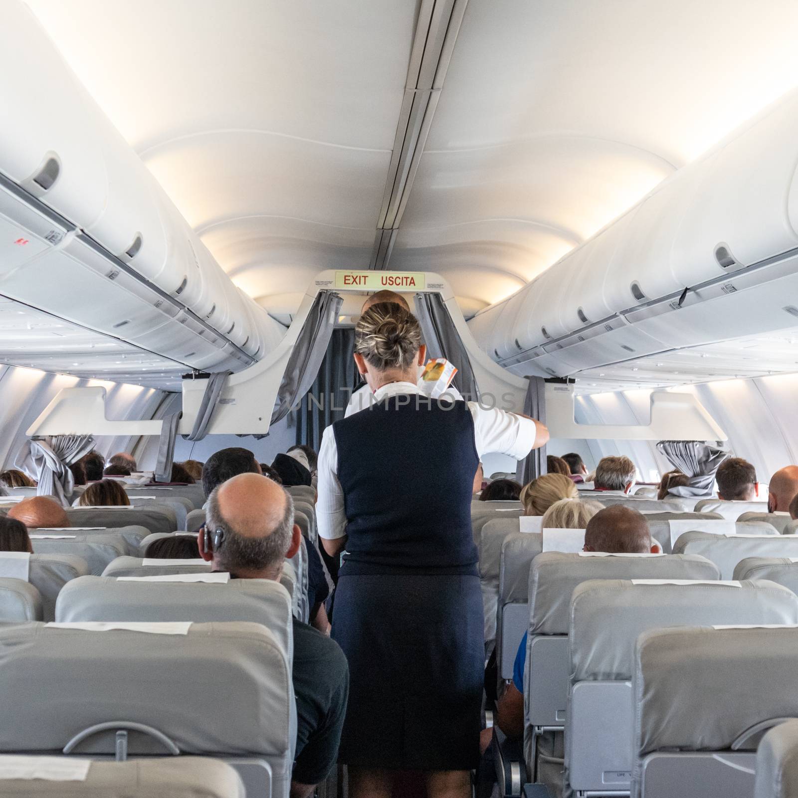 Interior of commercial airplane with stewardess serving passengers on seats during flight. by kasto