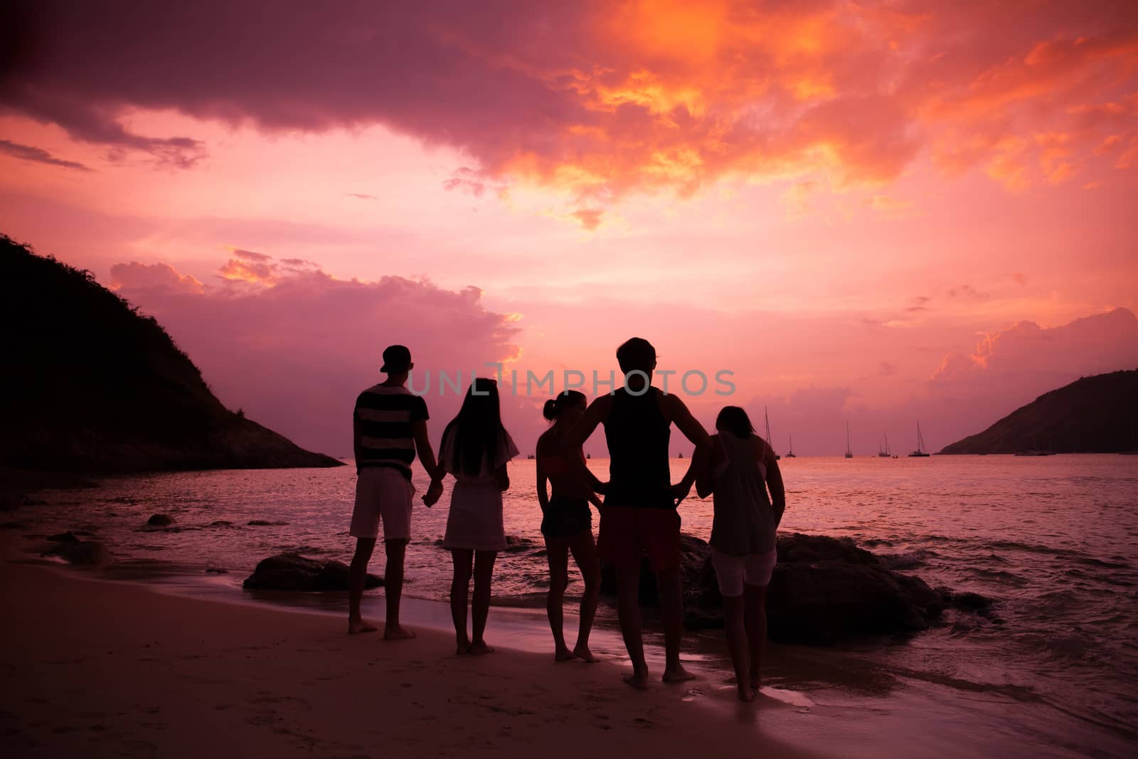 Group of happy people at sea beach at sunset