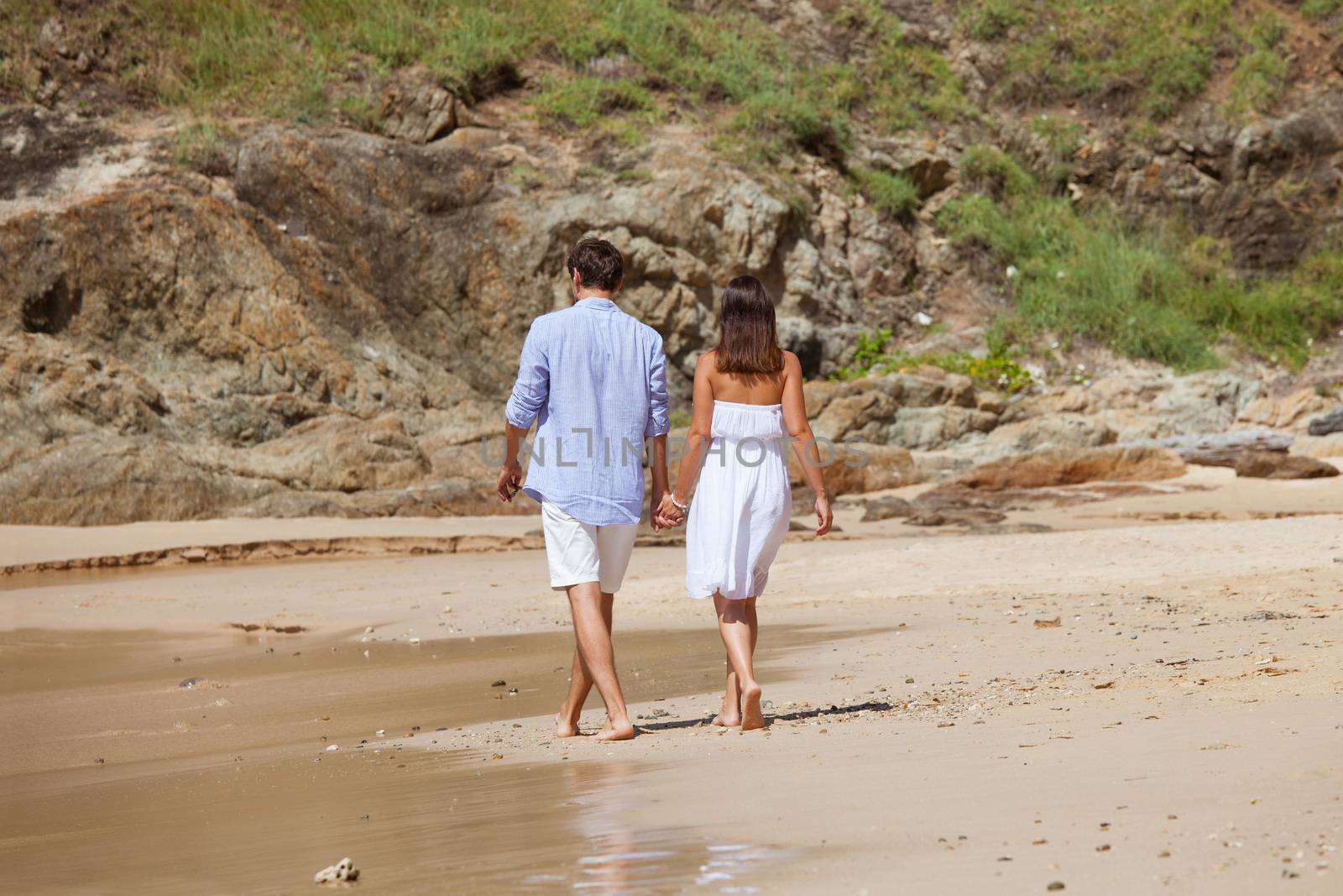 Happy couple walking on sand of tropical beach