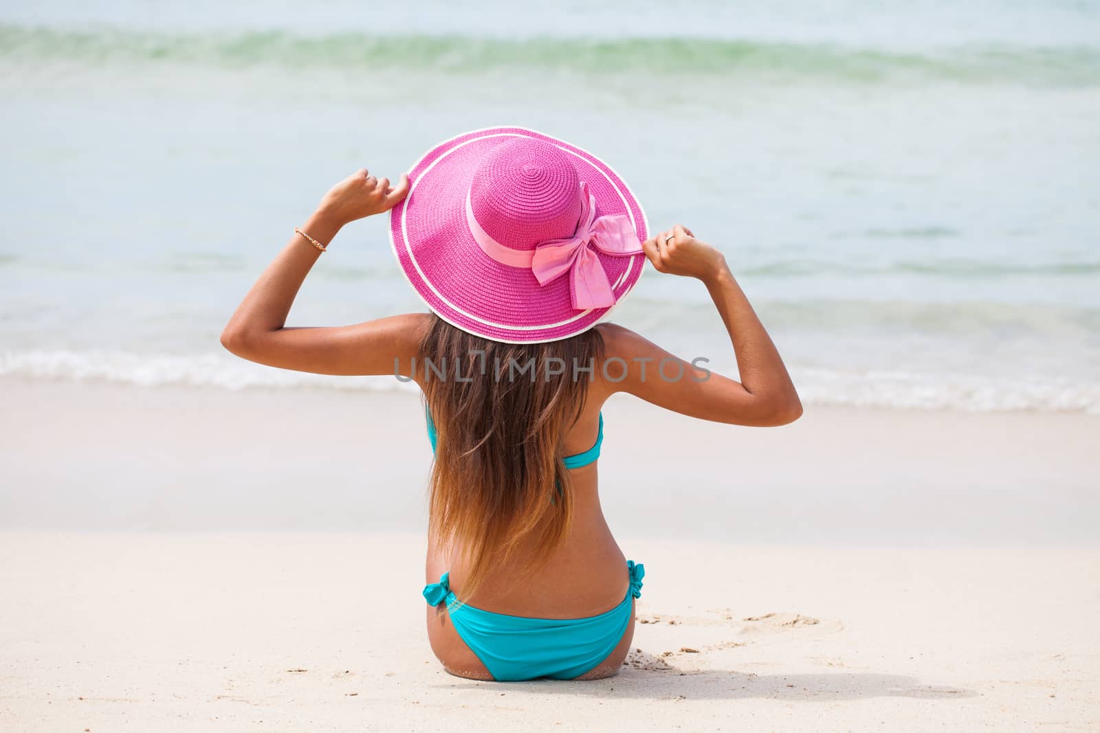 Travel woman on beach enjoying blue sea and sky wearing pink beach sun hat and bikini