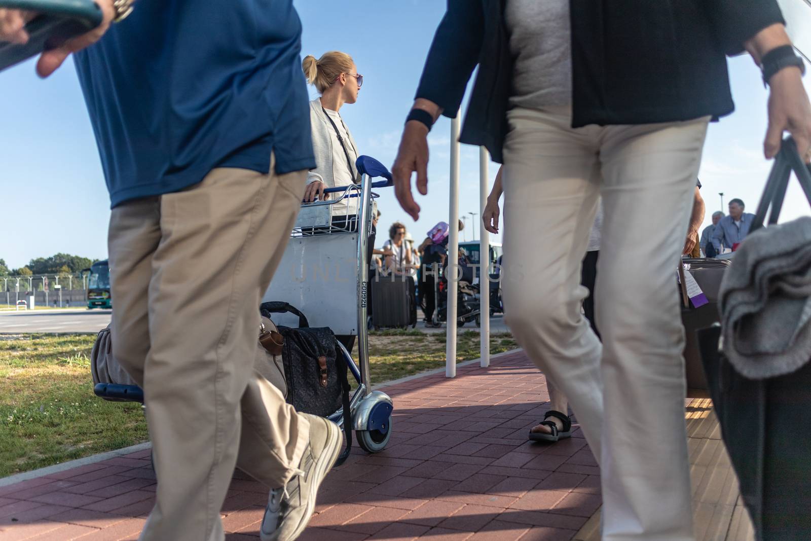 Young casual woman transporting luggage from arrival parking to international airport departure termainal by luggage trolley.