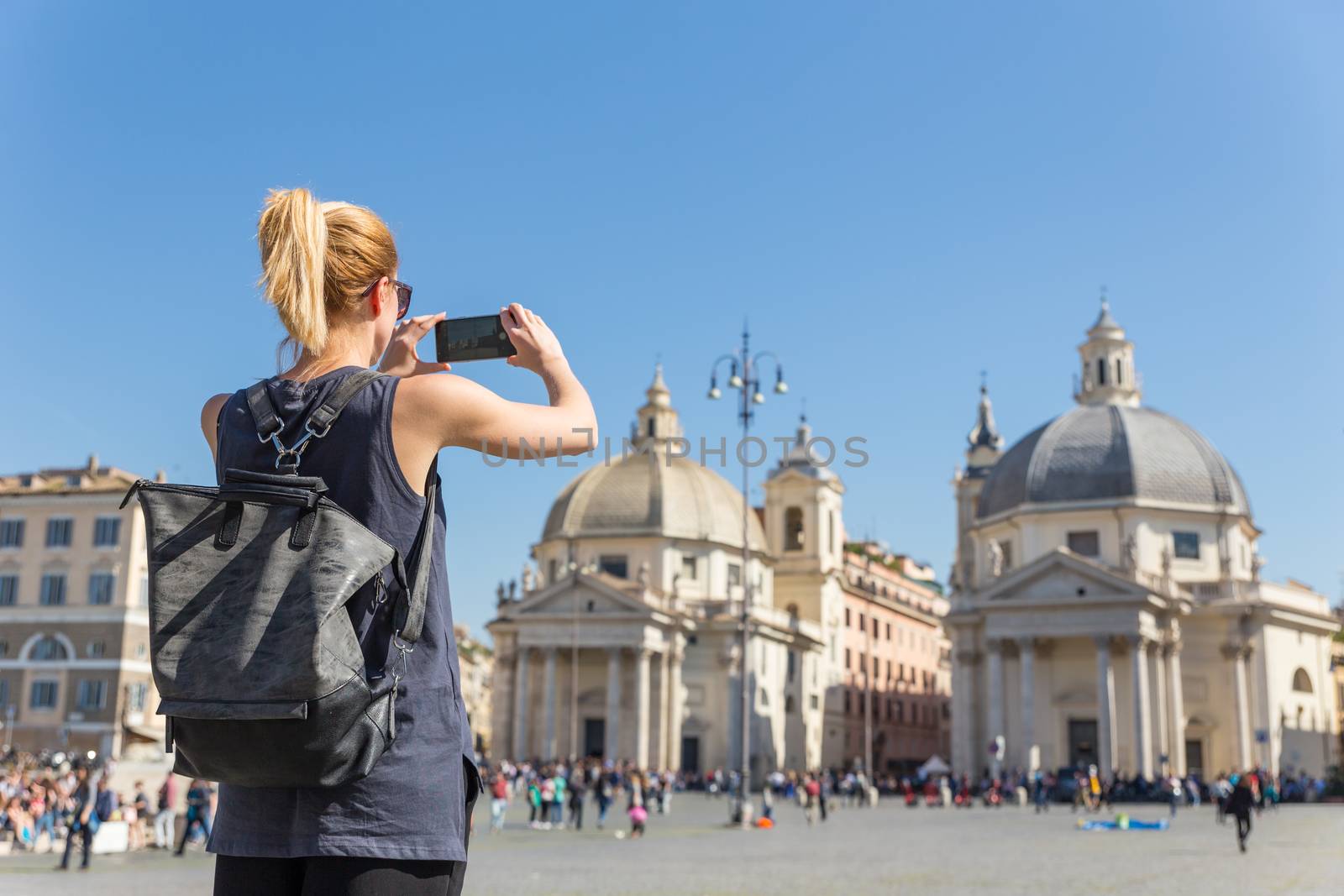 Female tourist with a fashinable vintage hipster backpack taking photo of Piazza del Popolo in Rome, Italy by her mobile phone. by kasto