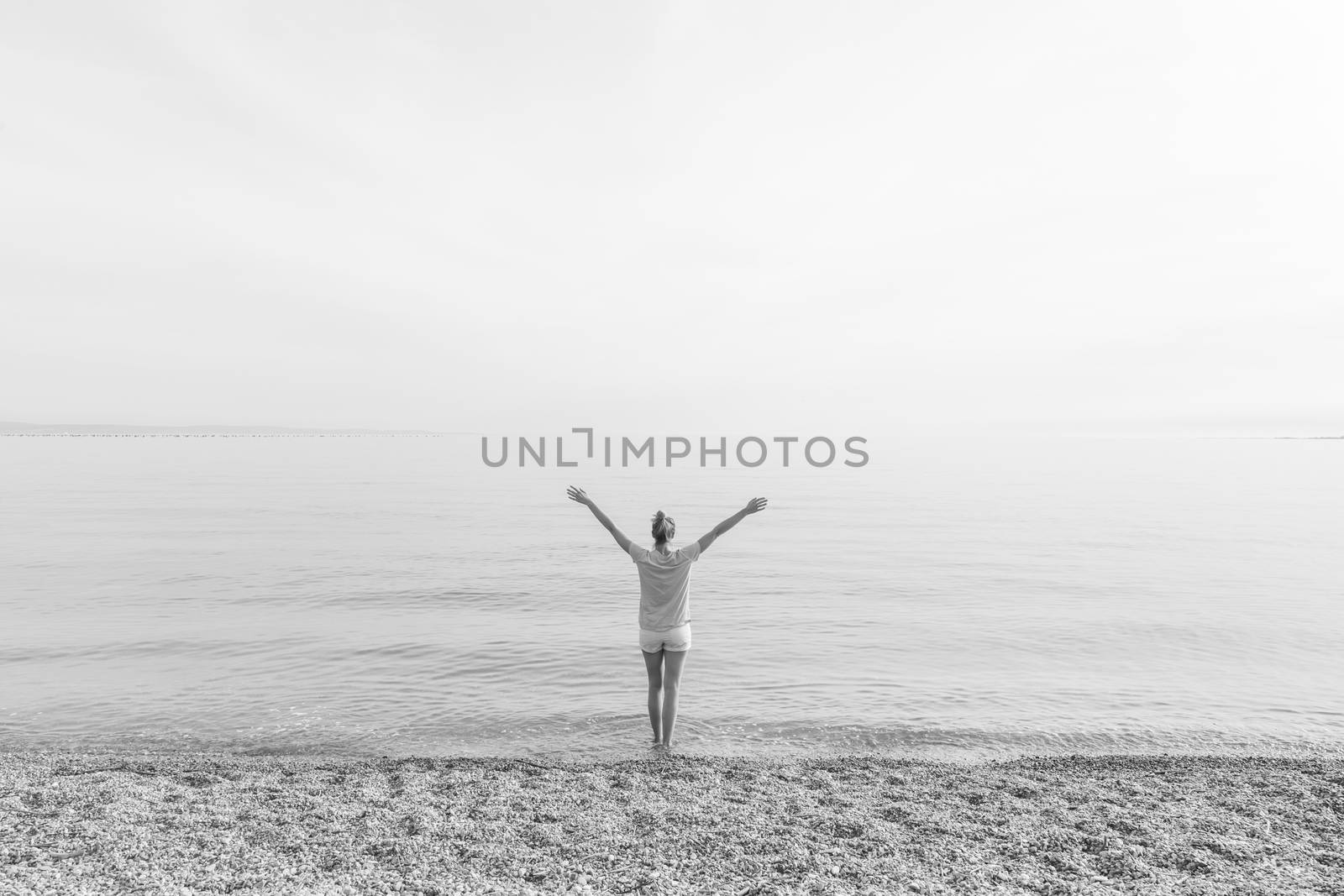 Happy Carefree Woman Enjoying Late Afternoon Walk on White Pabbled Beach in Summer.