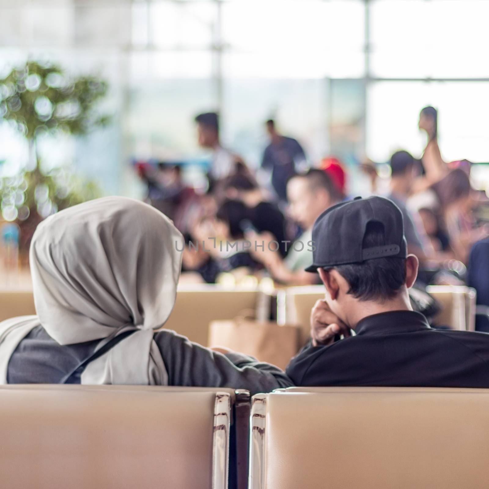 Modern muslim islamic asian couple sitting and waiting for flight departure at international airport terminal.