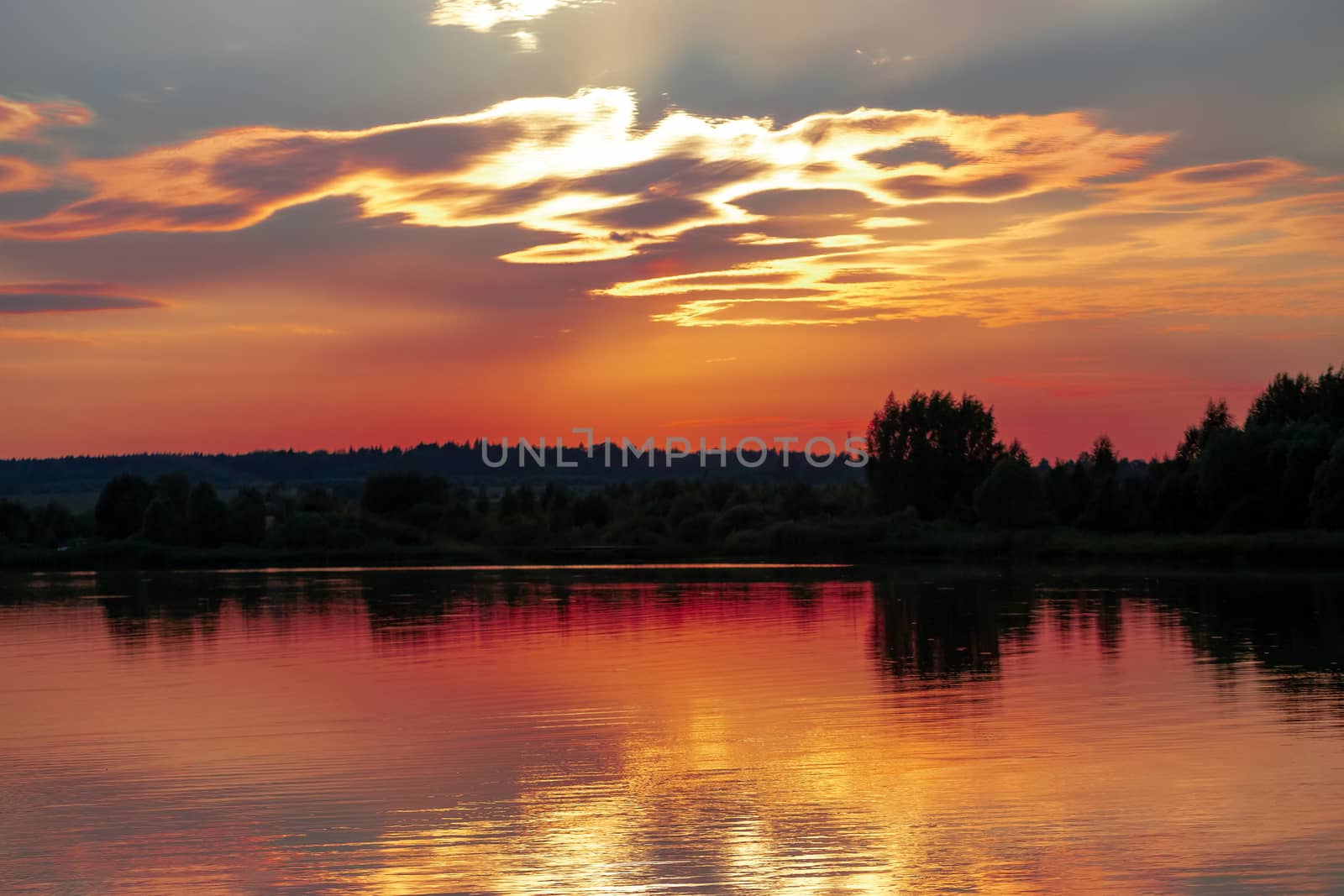 Panorama reflection of sunset in the water of the lake. The sky and clouds, illuminated by the sun setting over the horizon, acquired unusual red, orange and gray colors.
