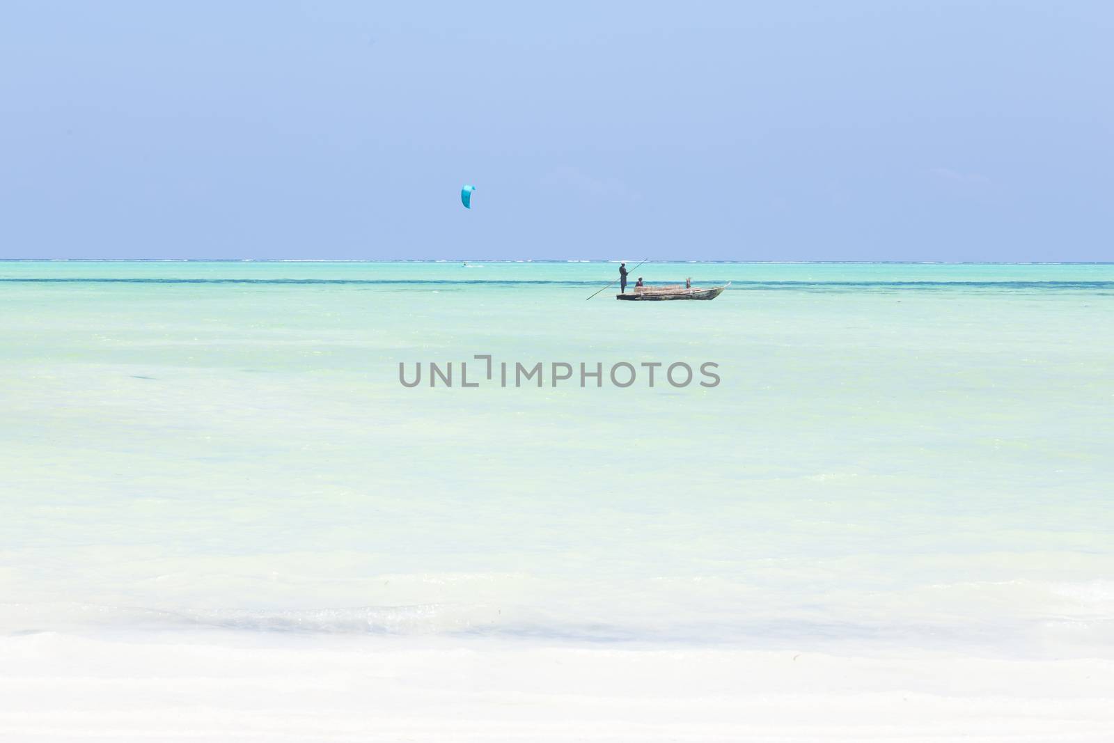 Solitary fishing boat and a kite surfer on picture perfect white sandy beach with turquoise blue sea, Paje, Zanzibar, Tanzania. Copy space.