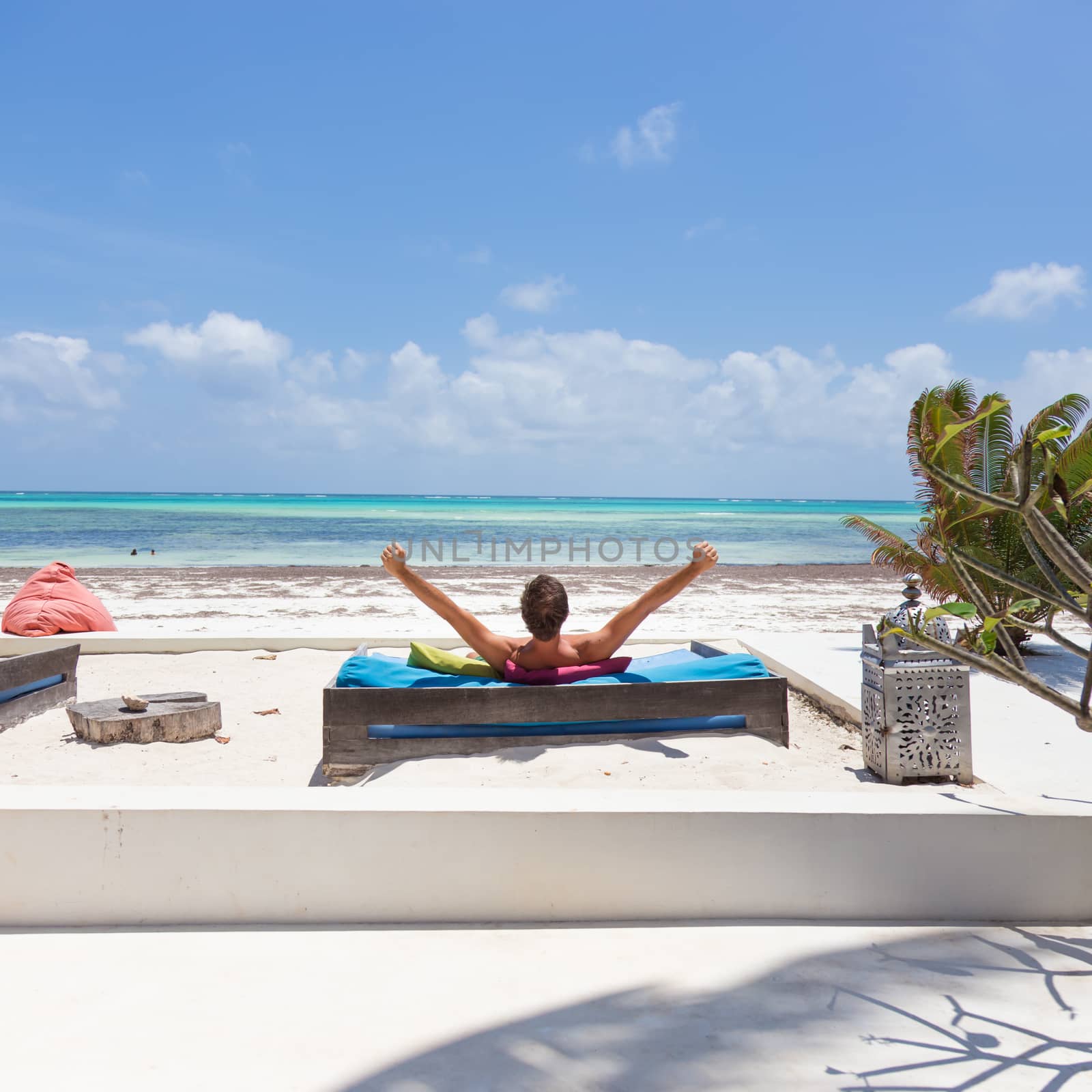 Relaxed man in luxury lounger, arms rised, enjoying summer vacations on beautiful beach. by kasto