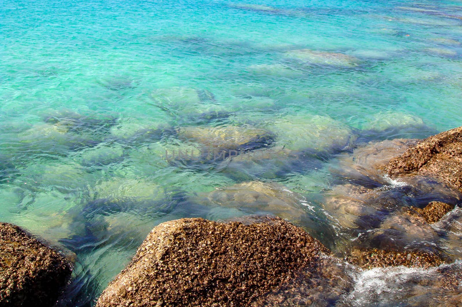 Sea water blue texture background, underwater stones. Wallpaper of clear blue tropical sea water with rocks under surface.