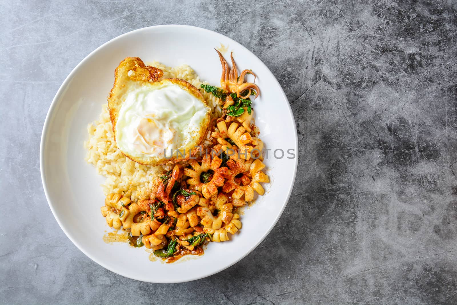 Spicy stir fried squid with basil leaves and chili, Sunny side up egg, served with brown rice. Hot and spicy dish.