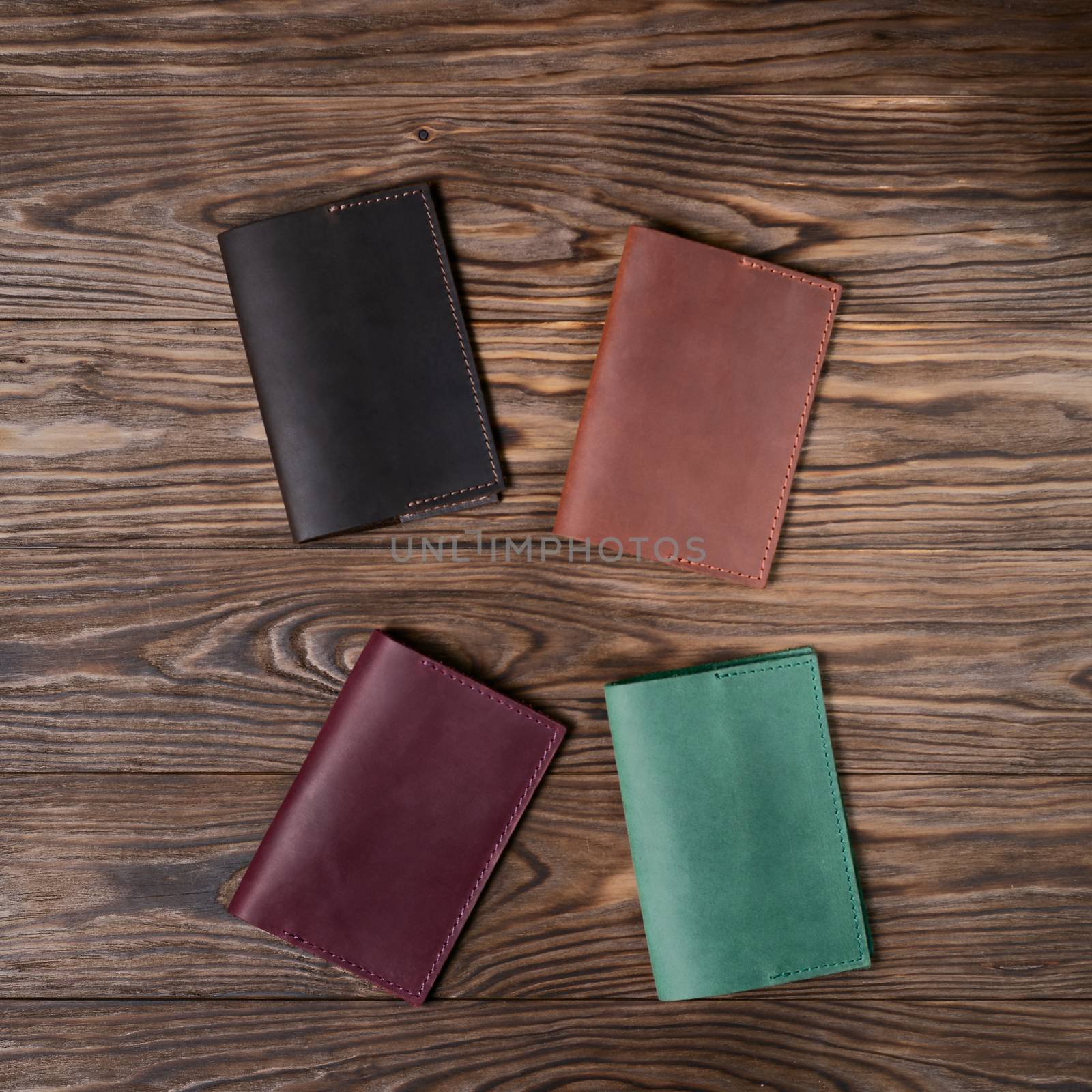 Four handmade leather passport covers on wooden textured background. Up to down view. Stock photo of luxury accessories. by alexsdriver