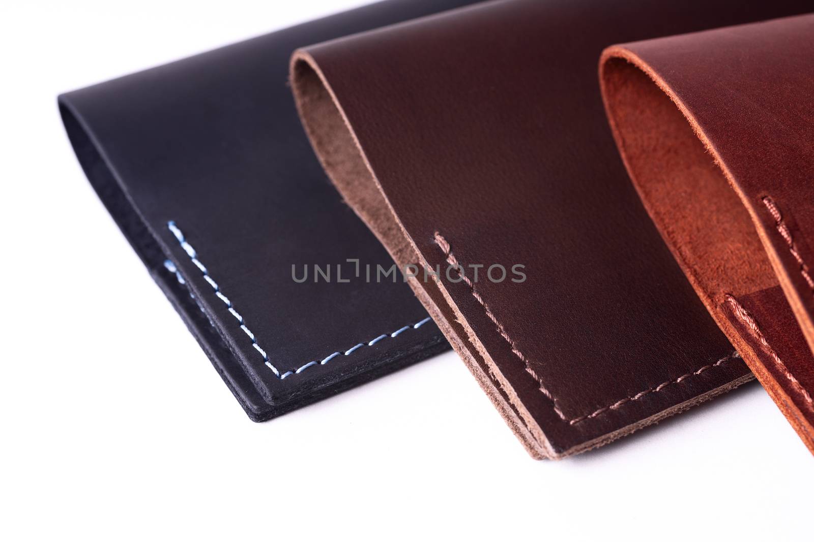 Three handmade leather passport covers isolated on white background. Covers are closed. Closeup view. Covers are dark blue, red and brown. by alexsdriver