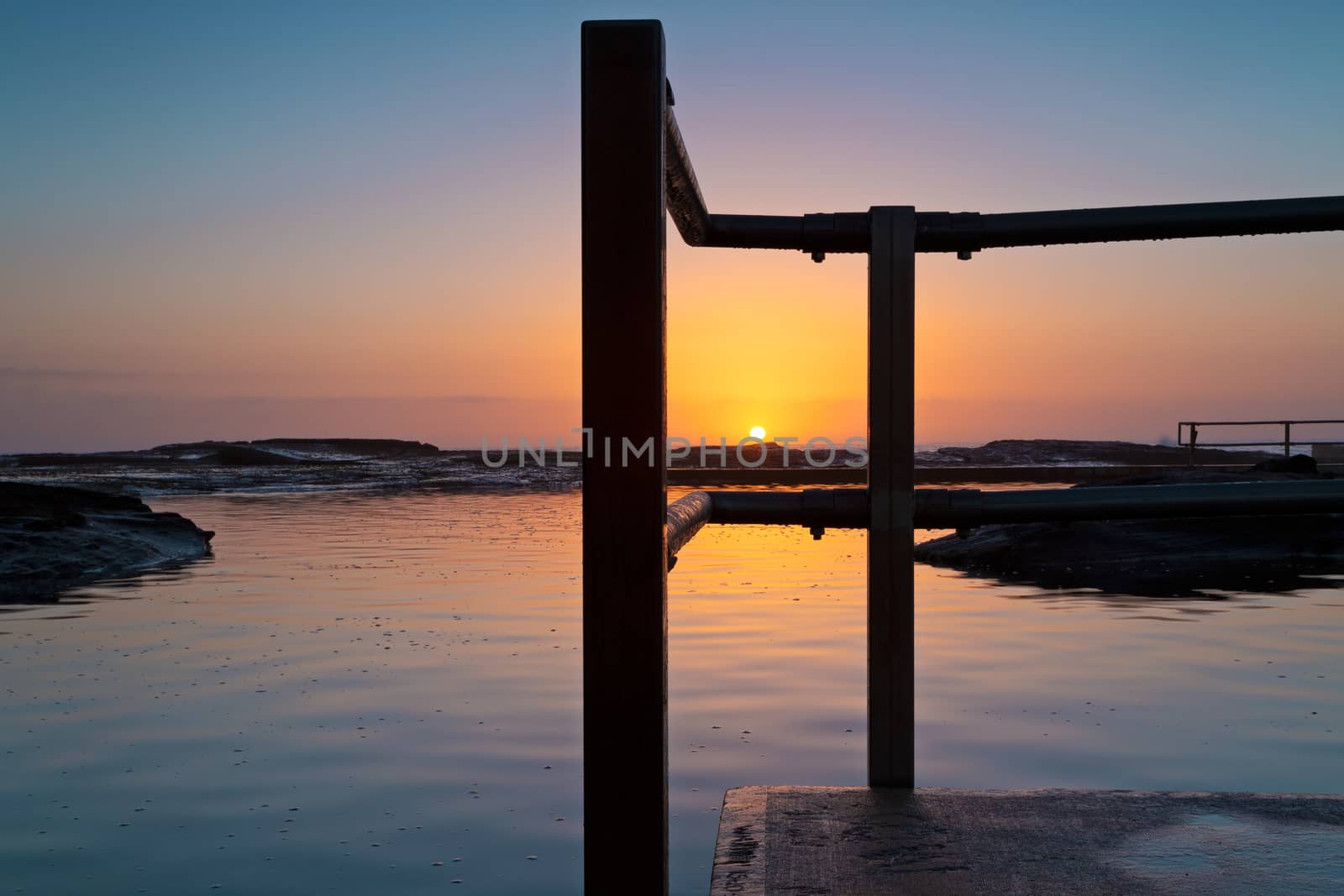 Glorious tranquil sunrise on the ocean horizon and ocean pool ripples and reflections. Location - North Curl Curl, nortthern beaches Sydney Australia