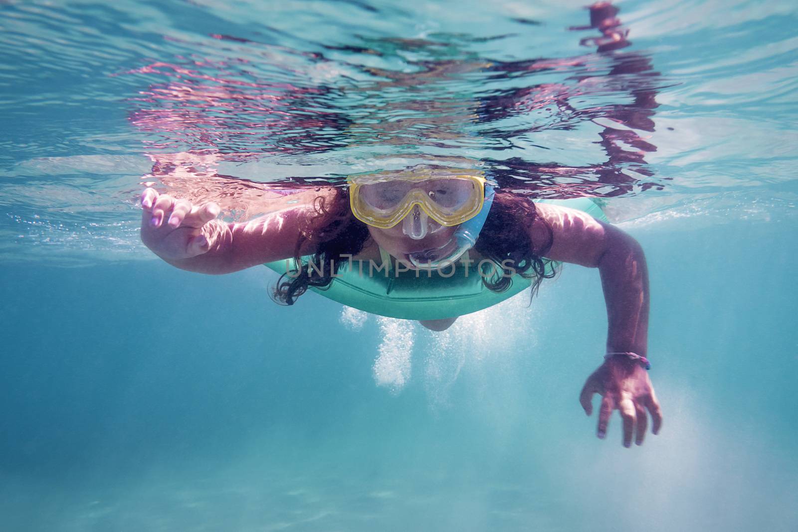 underwater photo of a little girl swimming in the sea with her glasses and snorkel, copy space for text
