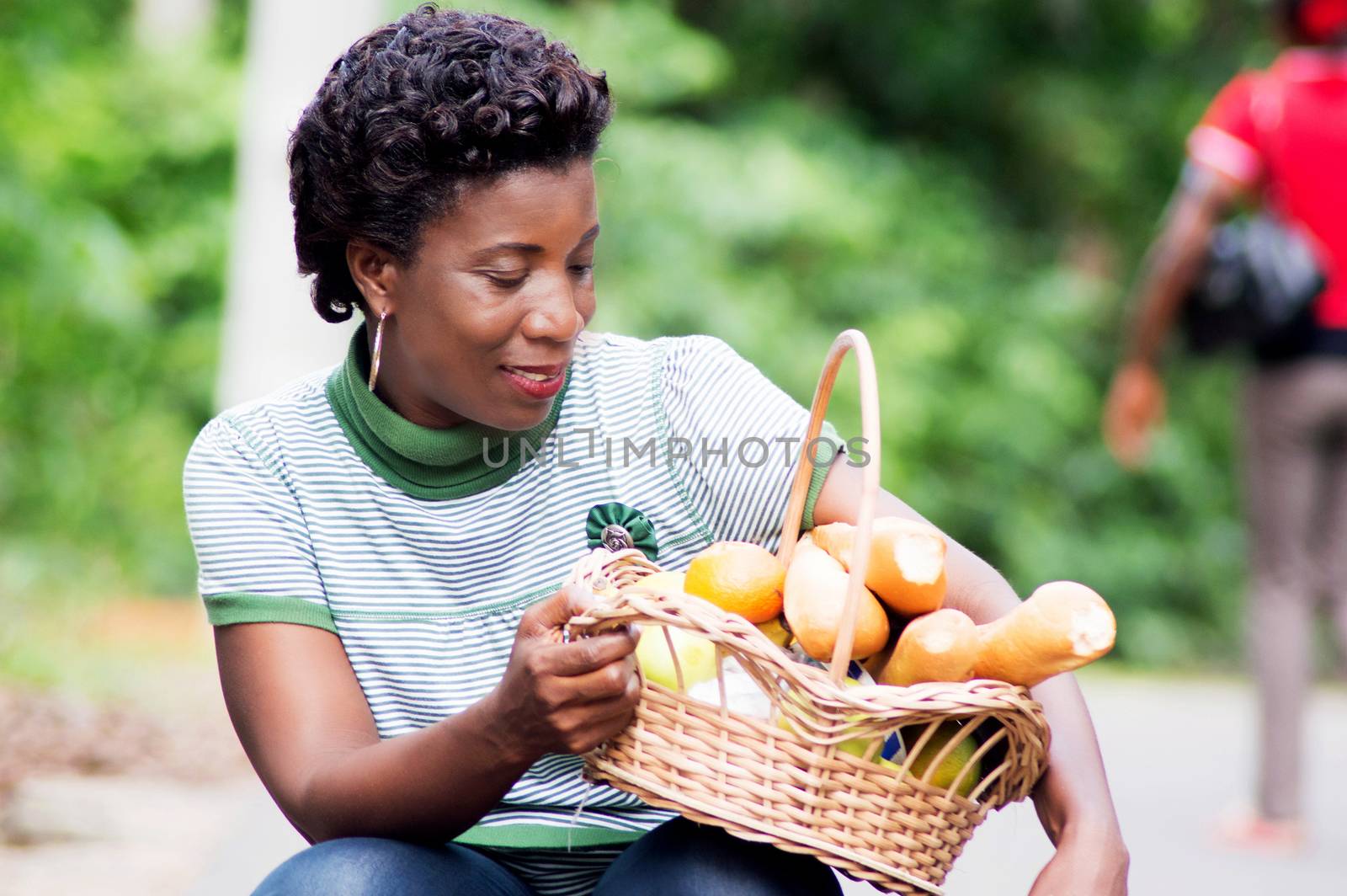 crouching young woman holds on his thigh a basket of food and look smiling.