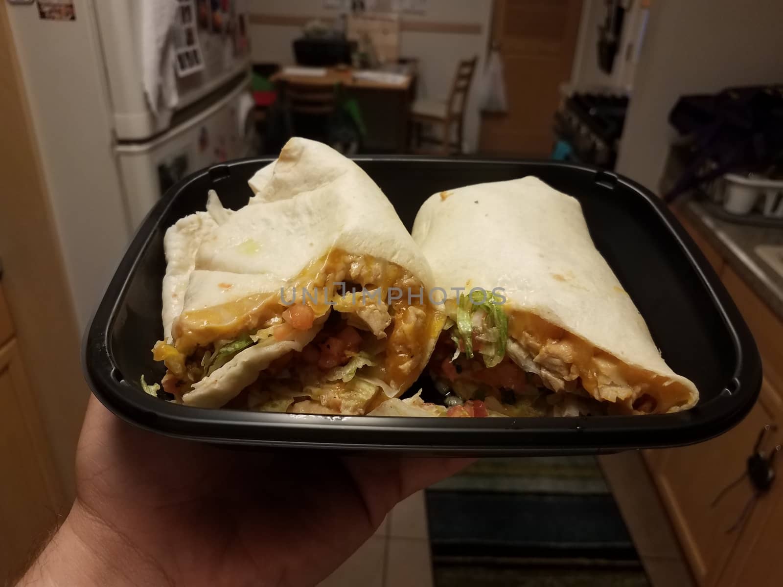 hand holding tortilla wrap with chicken and cheese in kitchen