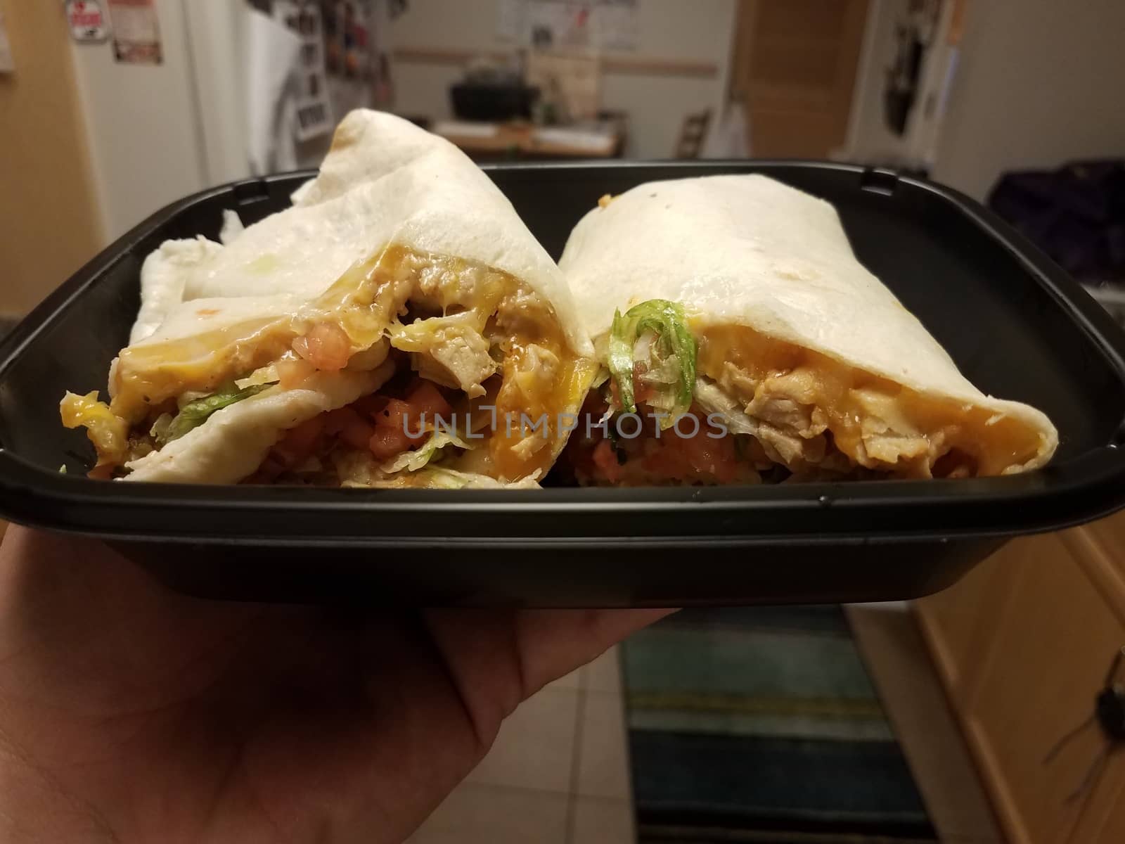 hand holding tortilla wrap with chicken and cheese in kitchen