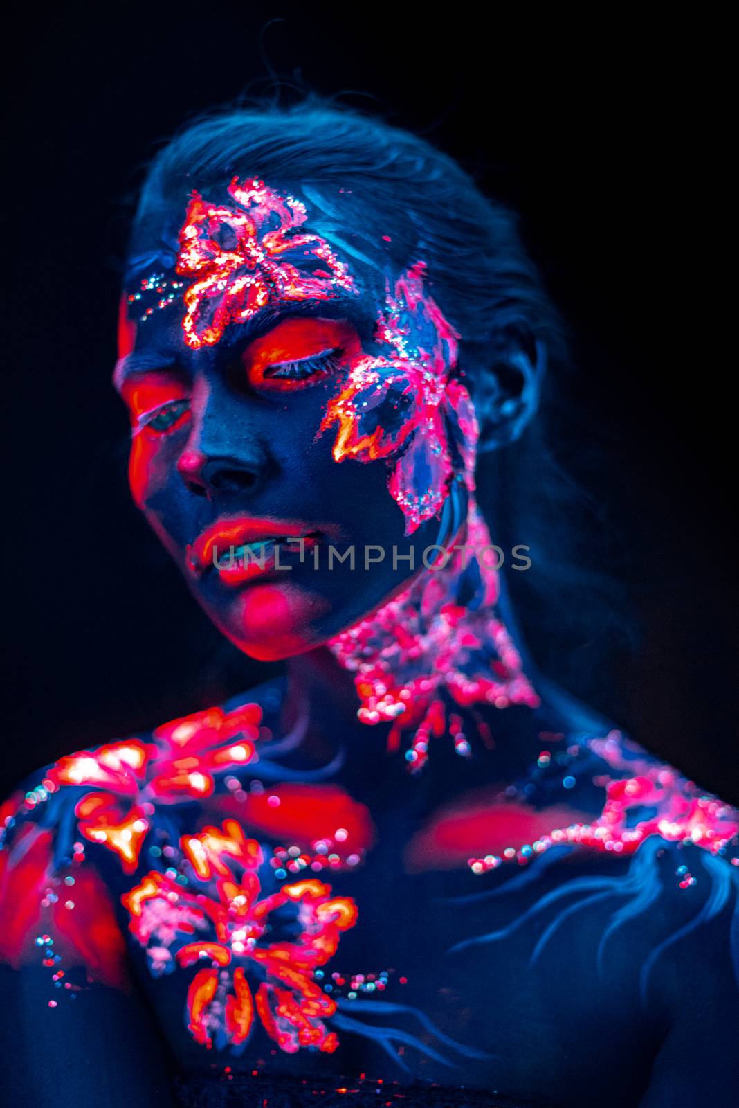 Conceptual face art with shining flowers painted in fluorescent colors isolated on black background