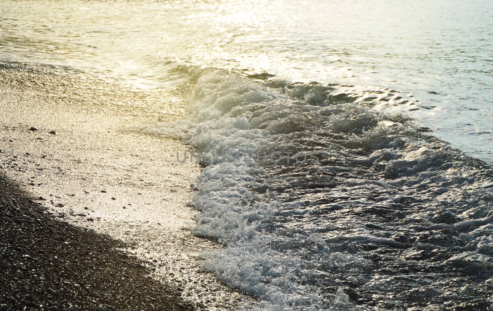 Shiny silver water on the sea pebble beach, early morning sunrise.