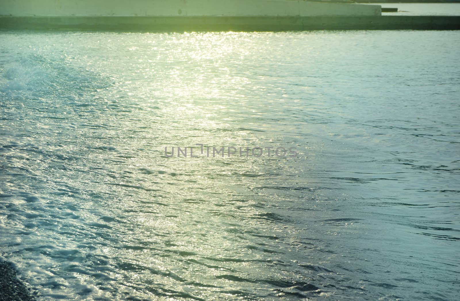 Shiny silver water on the sea pebble beach, early morning sunrise.