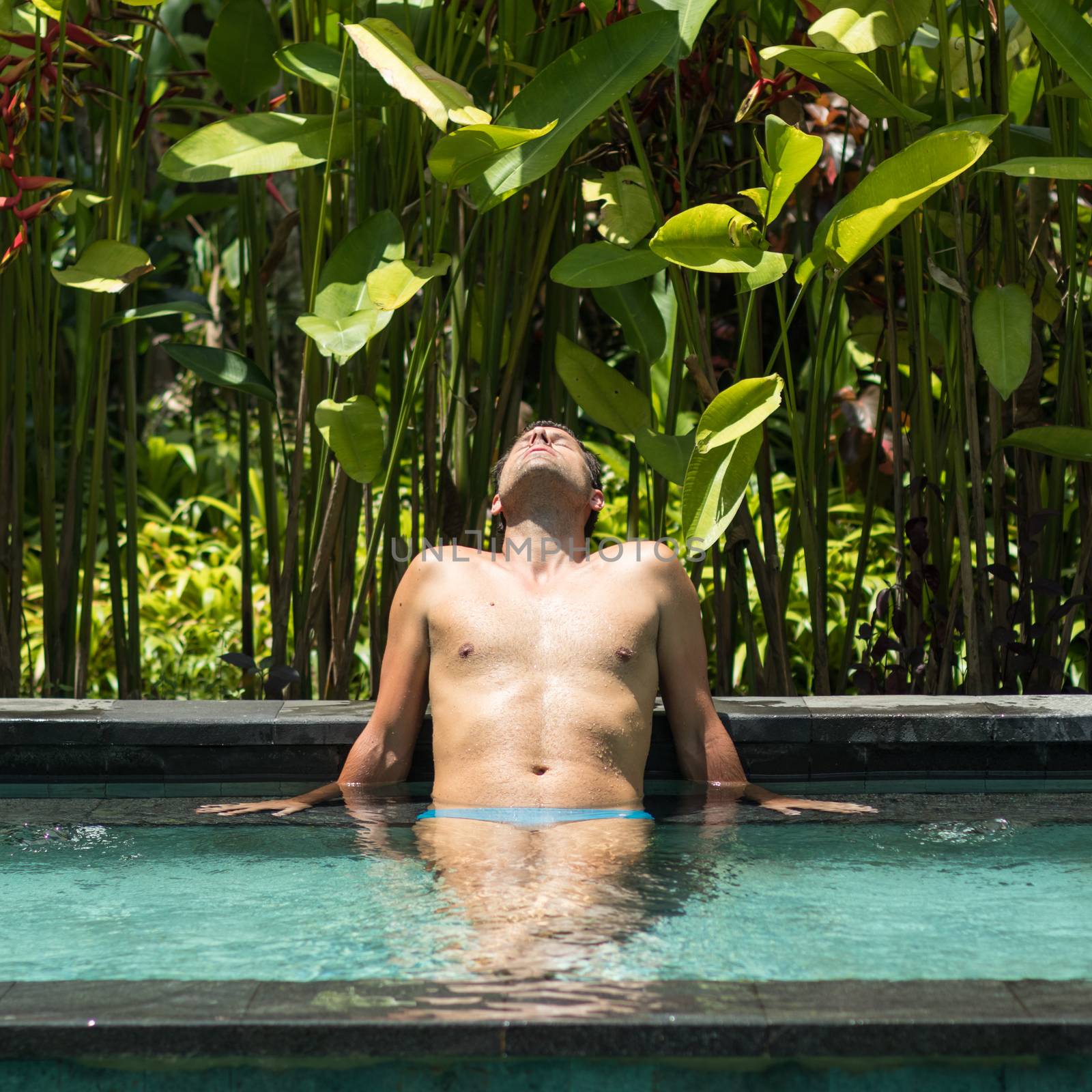 Man relaxing in outdoor spa infinity swimming pool surrounded with lush tropical greenery of Ubud, Bali. Male wellness, natural beauty and body care concept.
