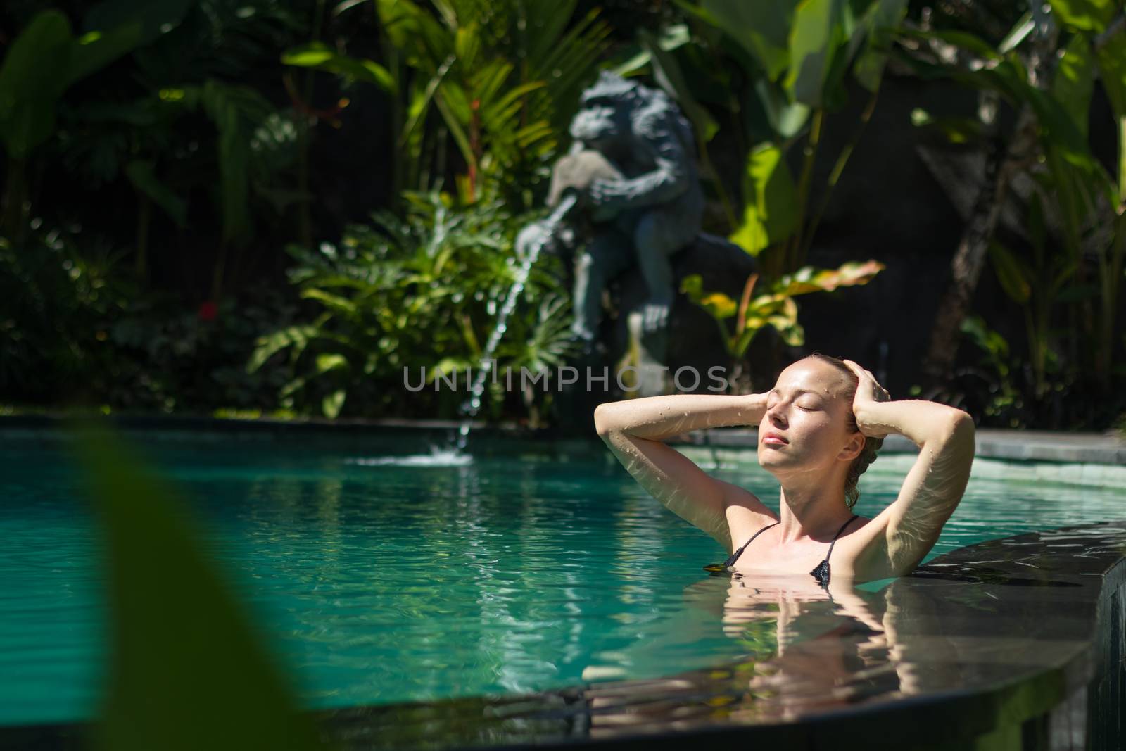Sensual young woman relaxing in outdoor spa infinity swimming pool surrounded with lush tropical greenery of Ubud, Bali. Wellness, natural beauty and body care concept.
